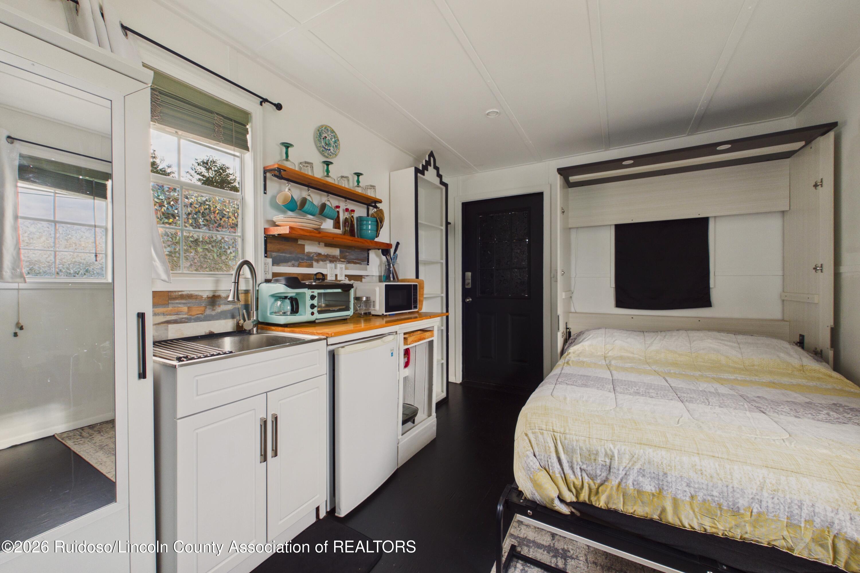 Furnished studio with a bed beside a compact kitchenette with wood counters and open shelves.