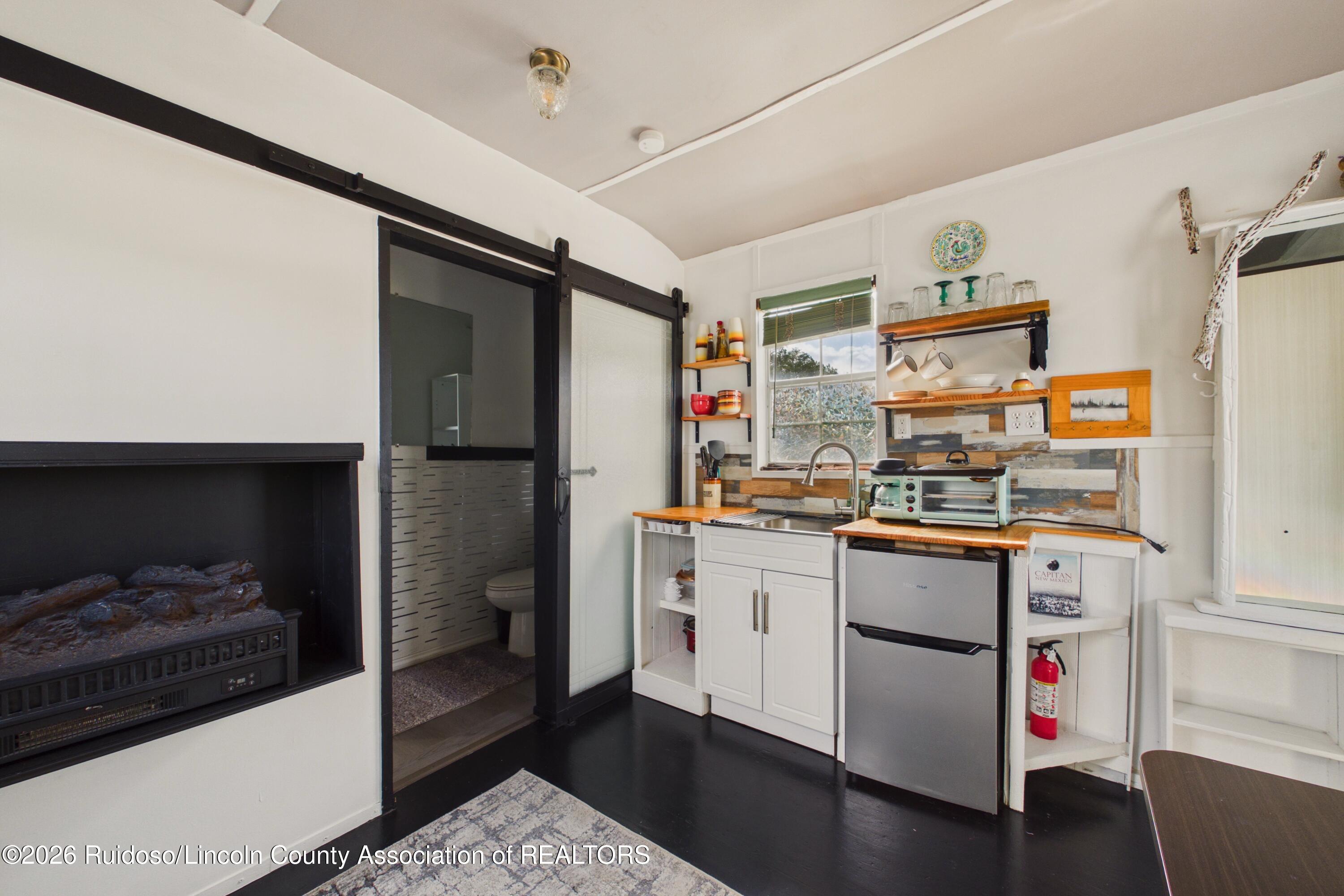 Compact kitchen with wood countertops, open shelving, a black fireplace, and a sliding barn door to the bathroom.