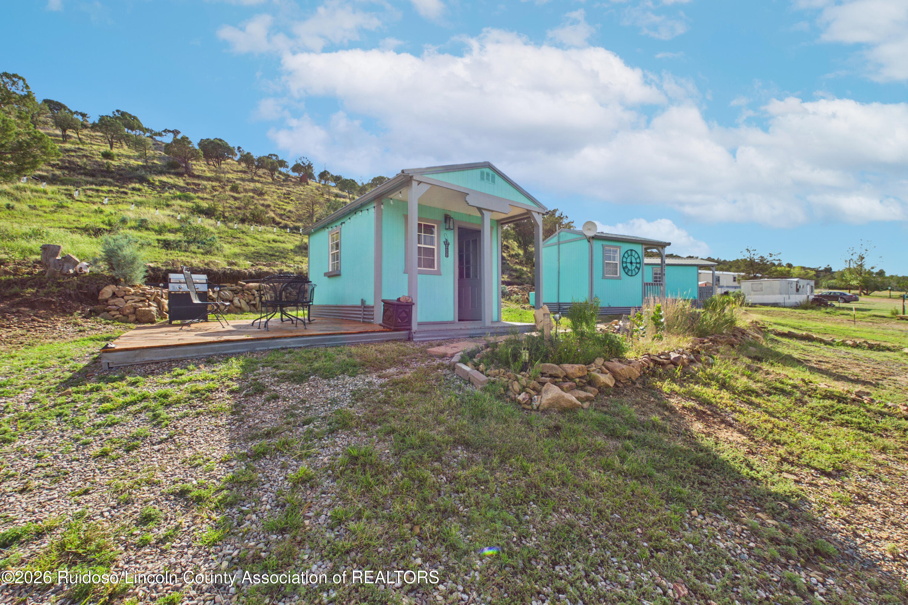 Turquoise buildings on a grassy hillside, with a wooden deck and outdoor seating.