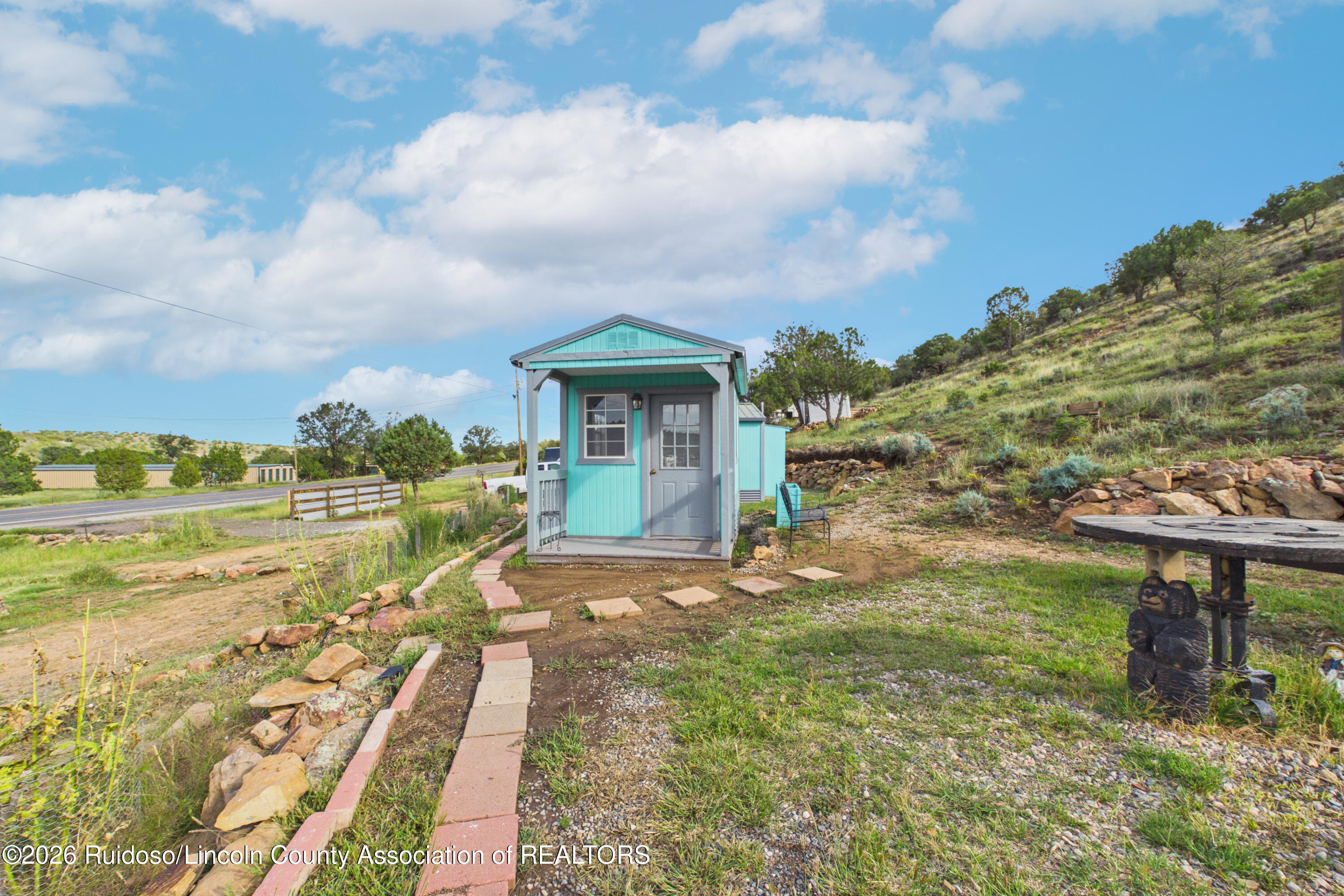 Small turquoise house with a covered porch and stepping-stone path on a grassy hillside.