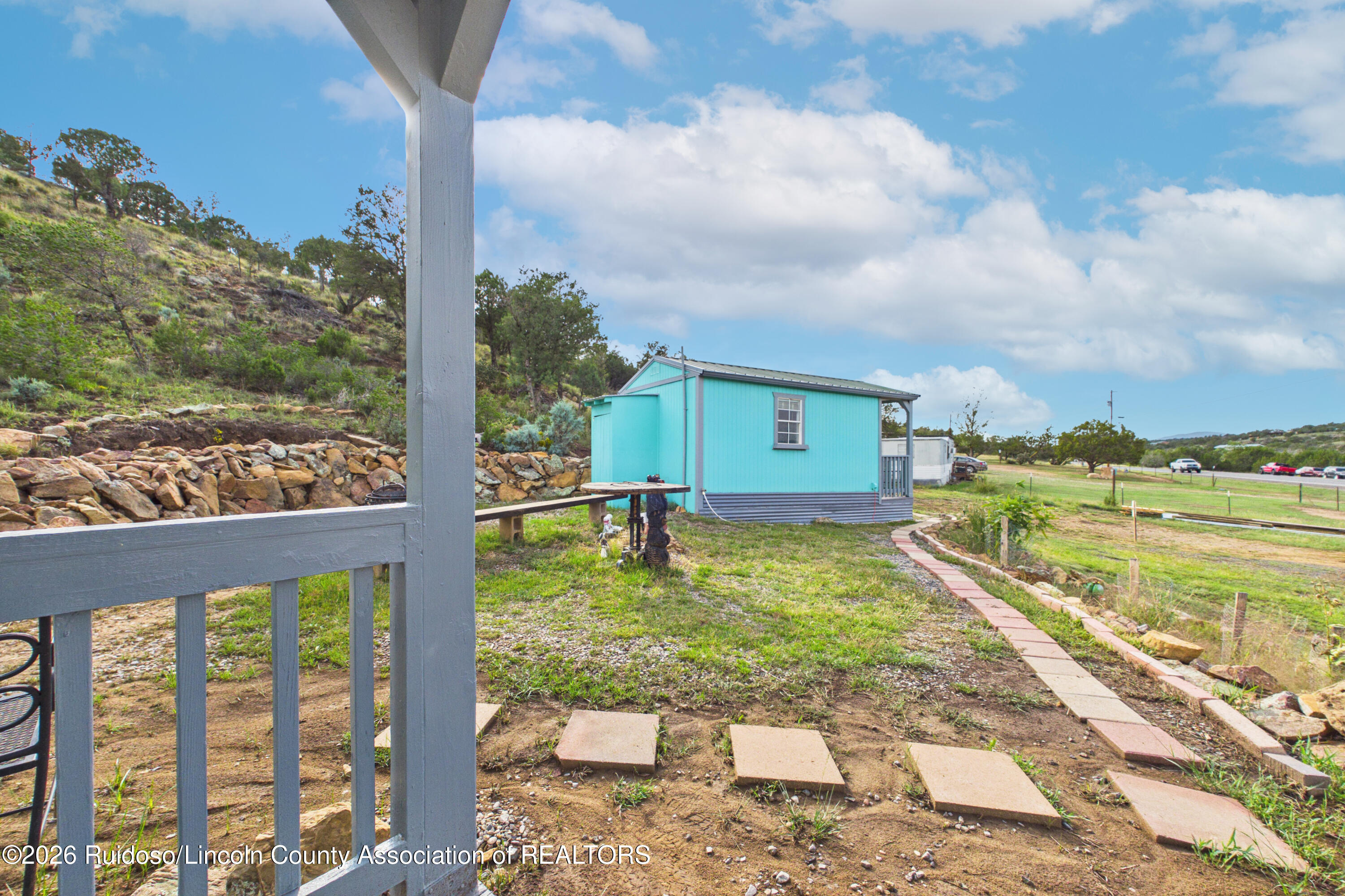 Turquoise outbuilding with a gray metal roof, stone retaining wall, and stepping-stone path.