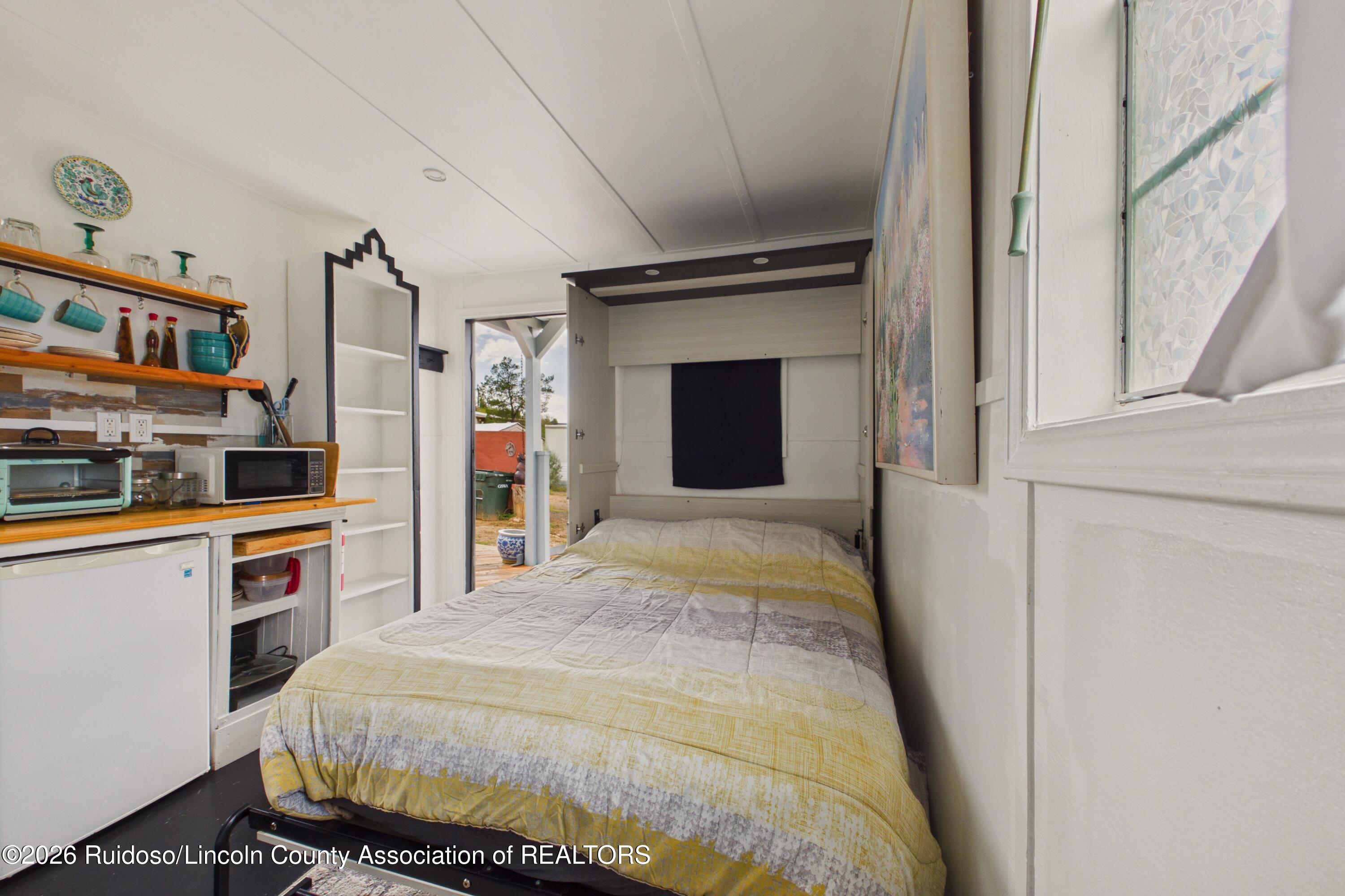 Compact bedroom with a double bed, fold-down wall bed cabinet, and kitchenette.