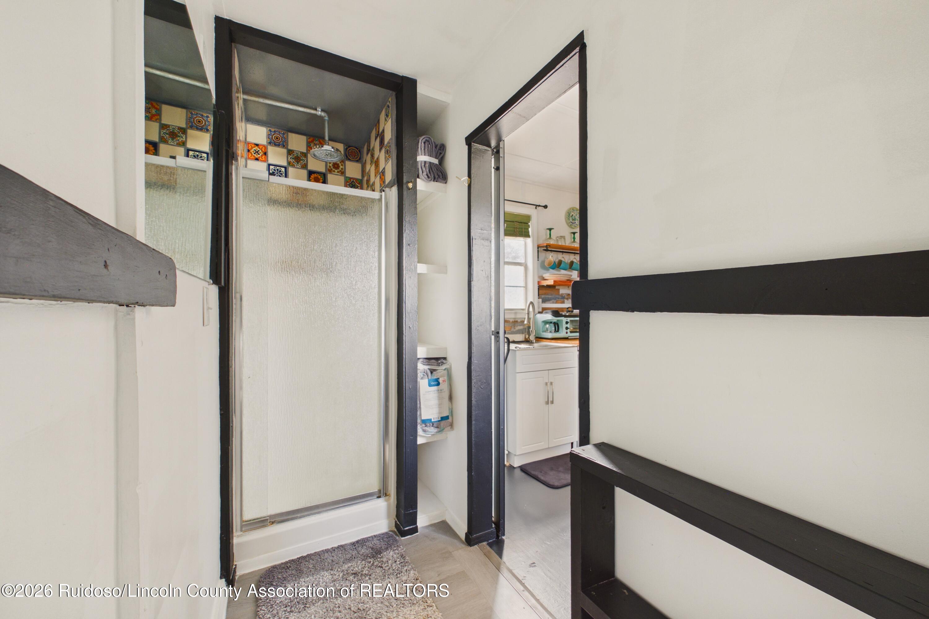 Bathroom shower with frosted glass doors and colorful patterned tile, with a glimpse of the kitchen.