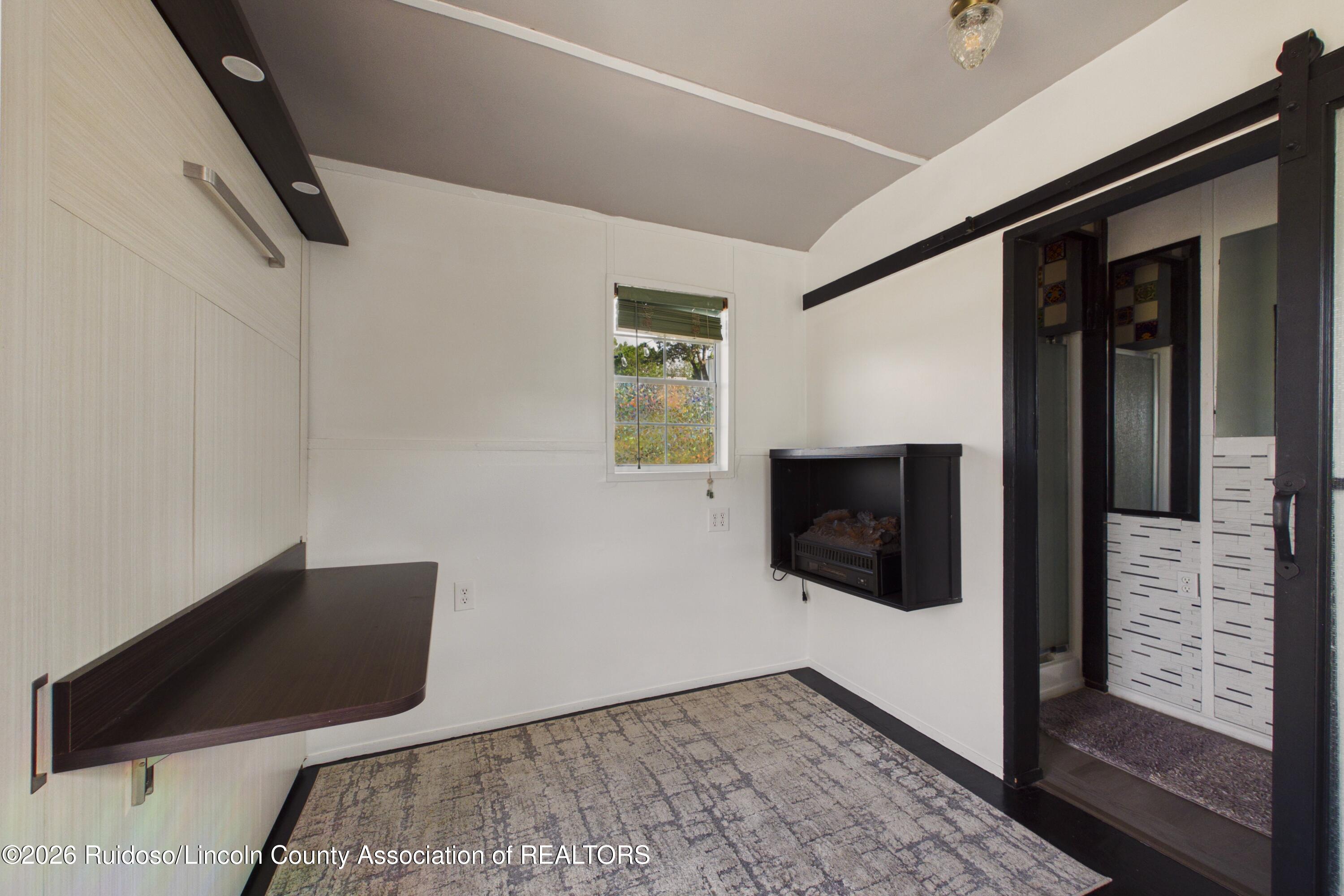 Office with a wall-mounted desk, electric fireplace, and dark-trimmed doorway.