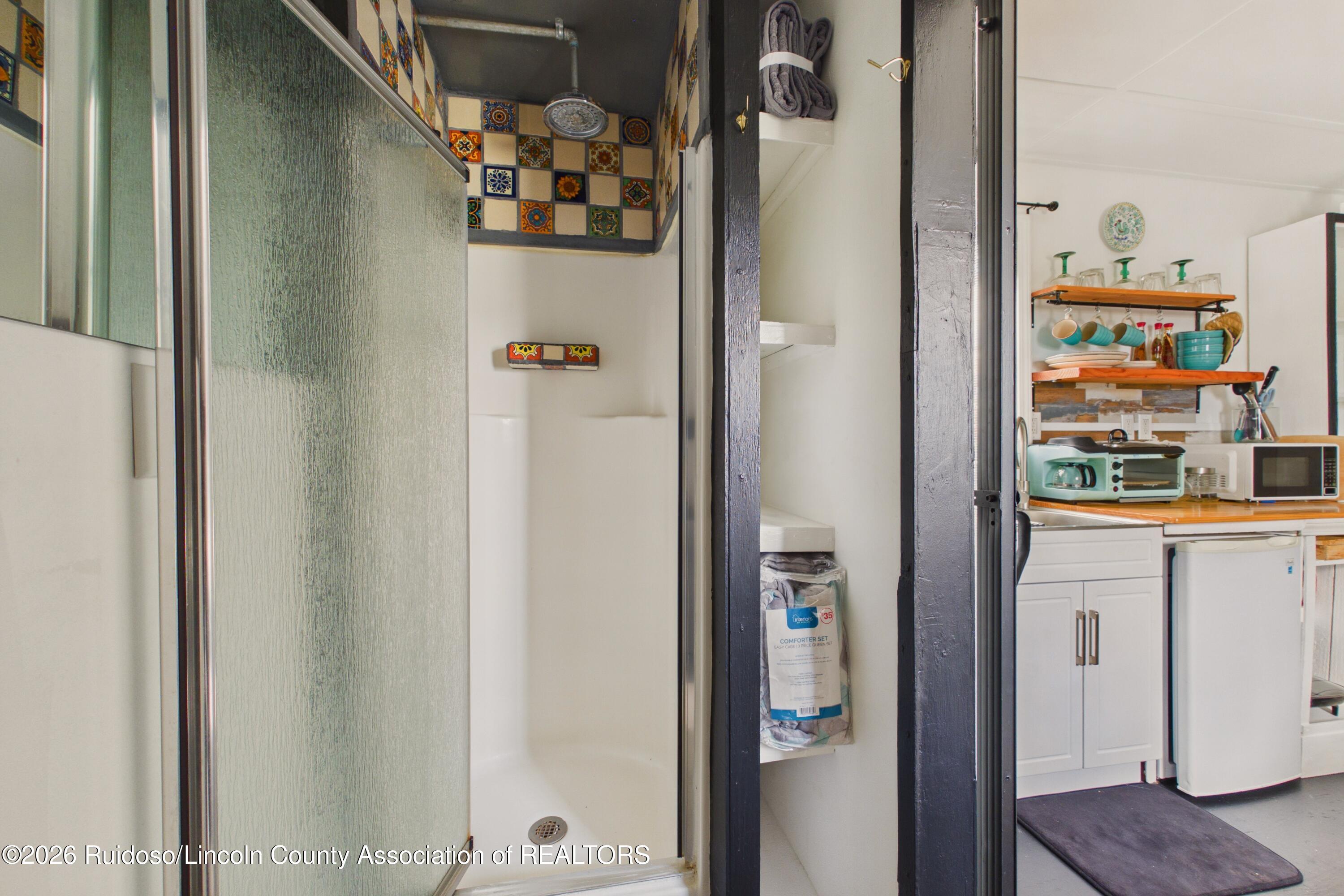 Bathroom with frosted-glass shower and colorful tile beside a kitchenette with open shelves and small appliances.