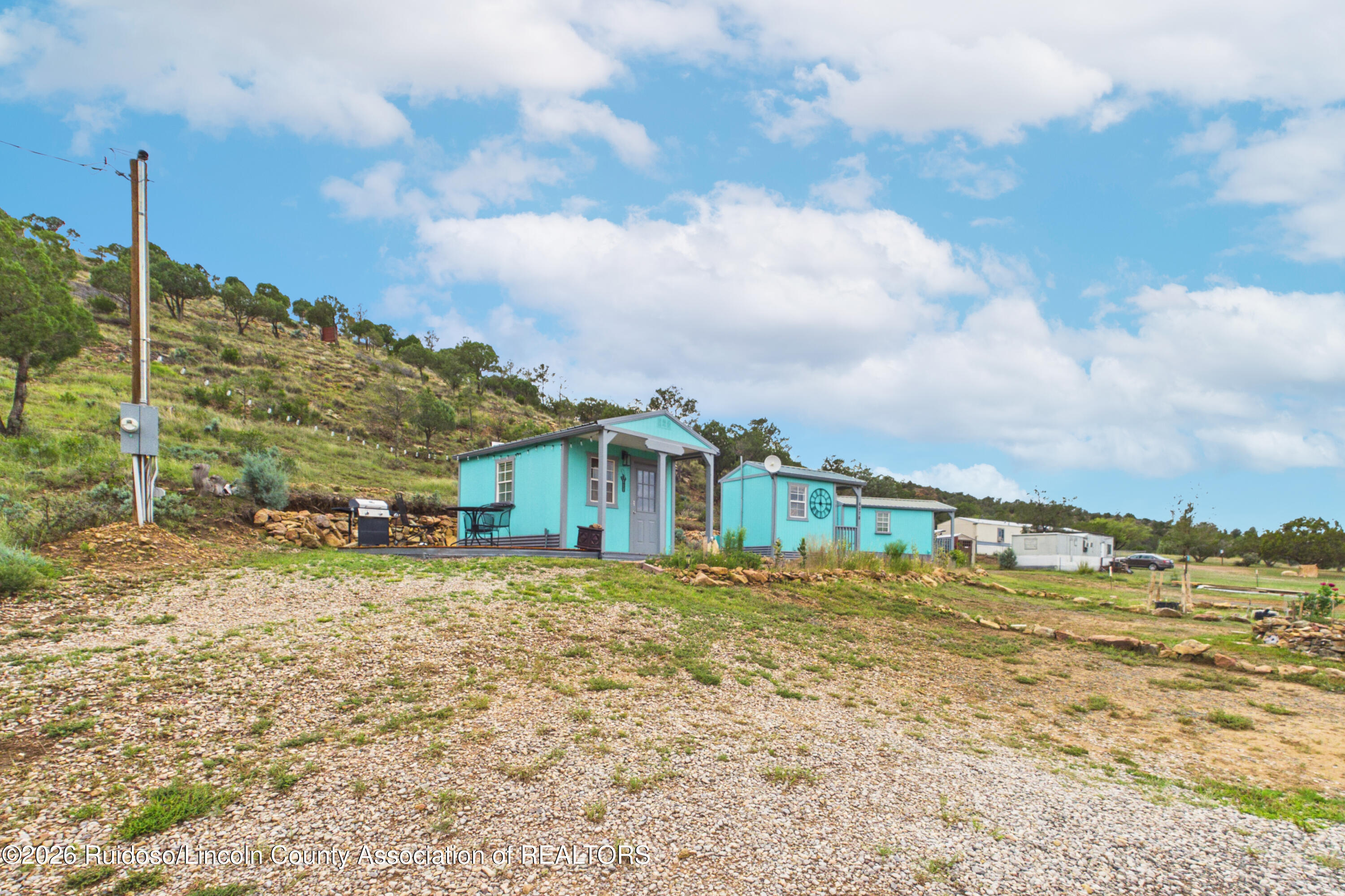Turquoise buildings on a gravel lot below a tree-dotted hillside.