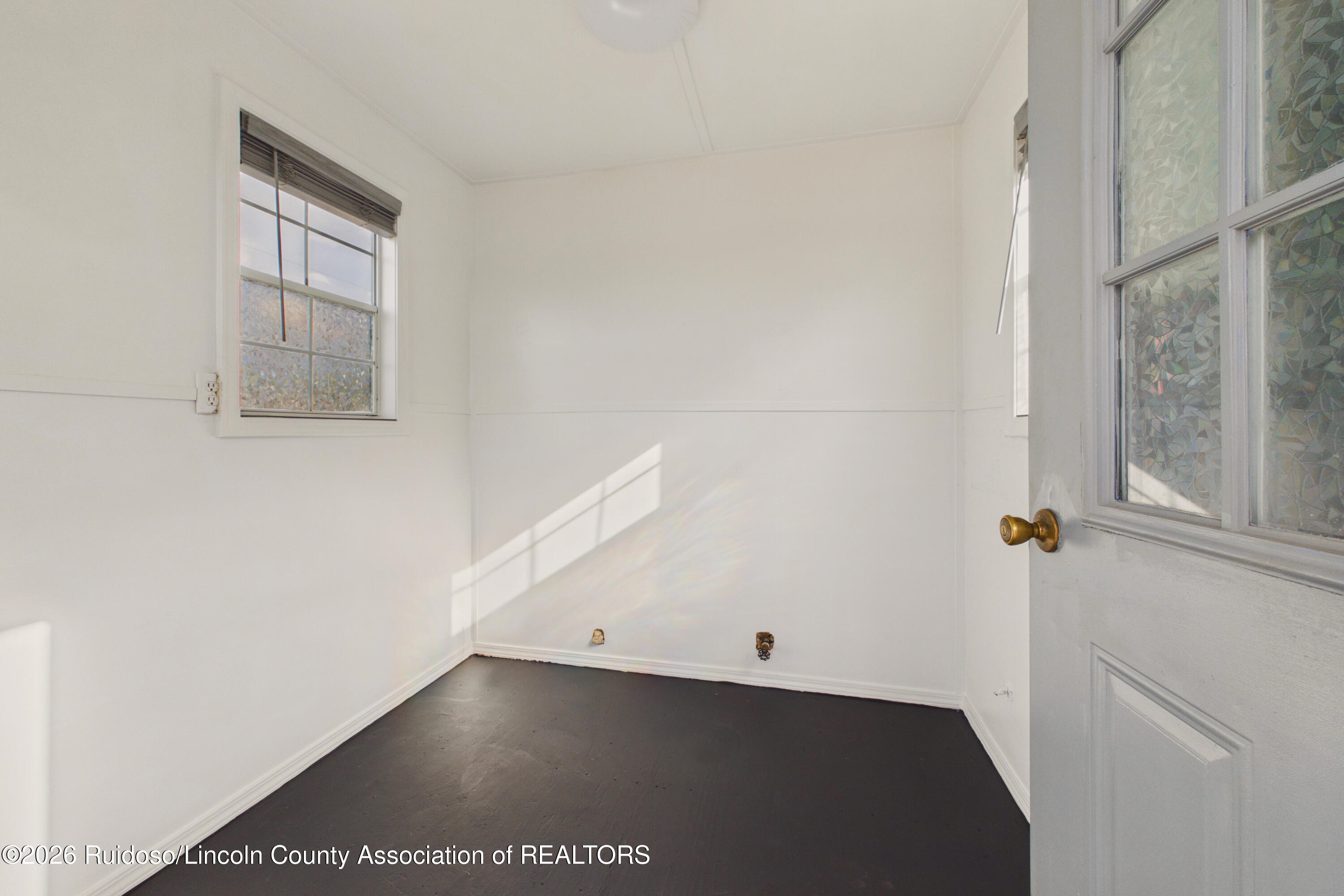 Empty room with white walls, a dark floor, a window with blinds, and a glass-paneled door.