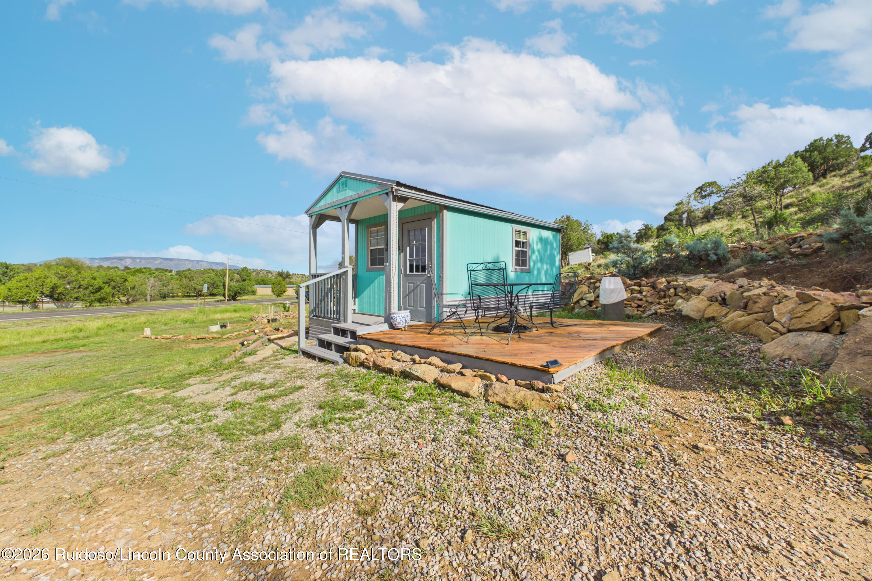 Turquoise cabin with a covered porch and wooden deck furnished with black metal chairs.