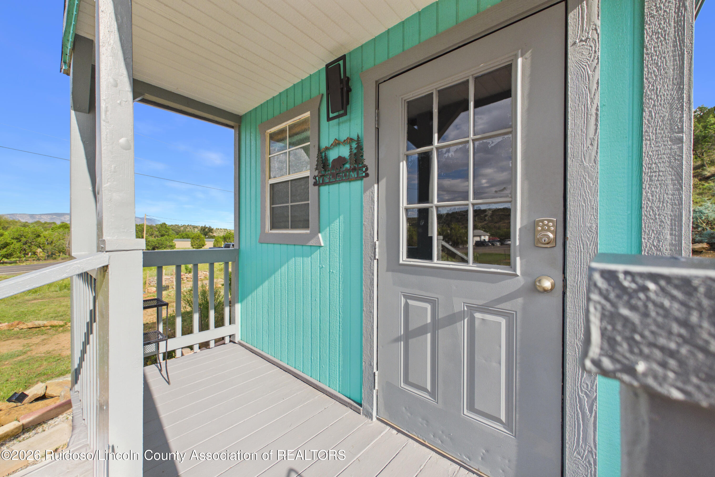 Turquoise-sided home entry with a gray glass-paneled door on a covered porch.