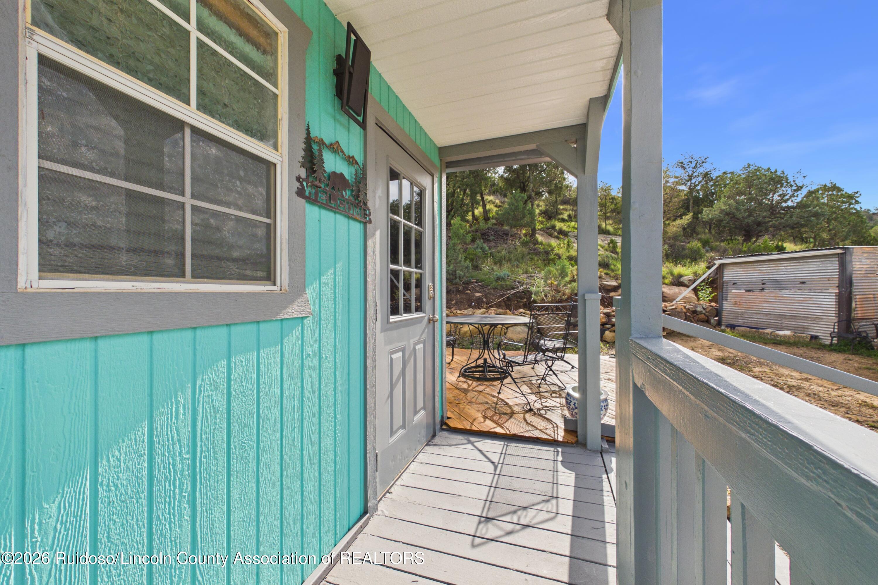 Covered porch with turquoise siding, metal patio furniture, and a wooded hillside beyond.