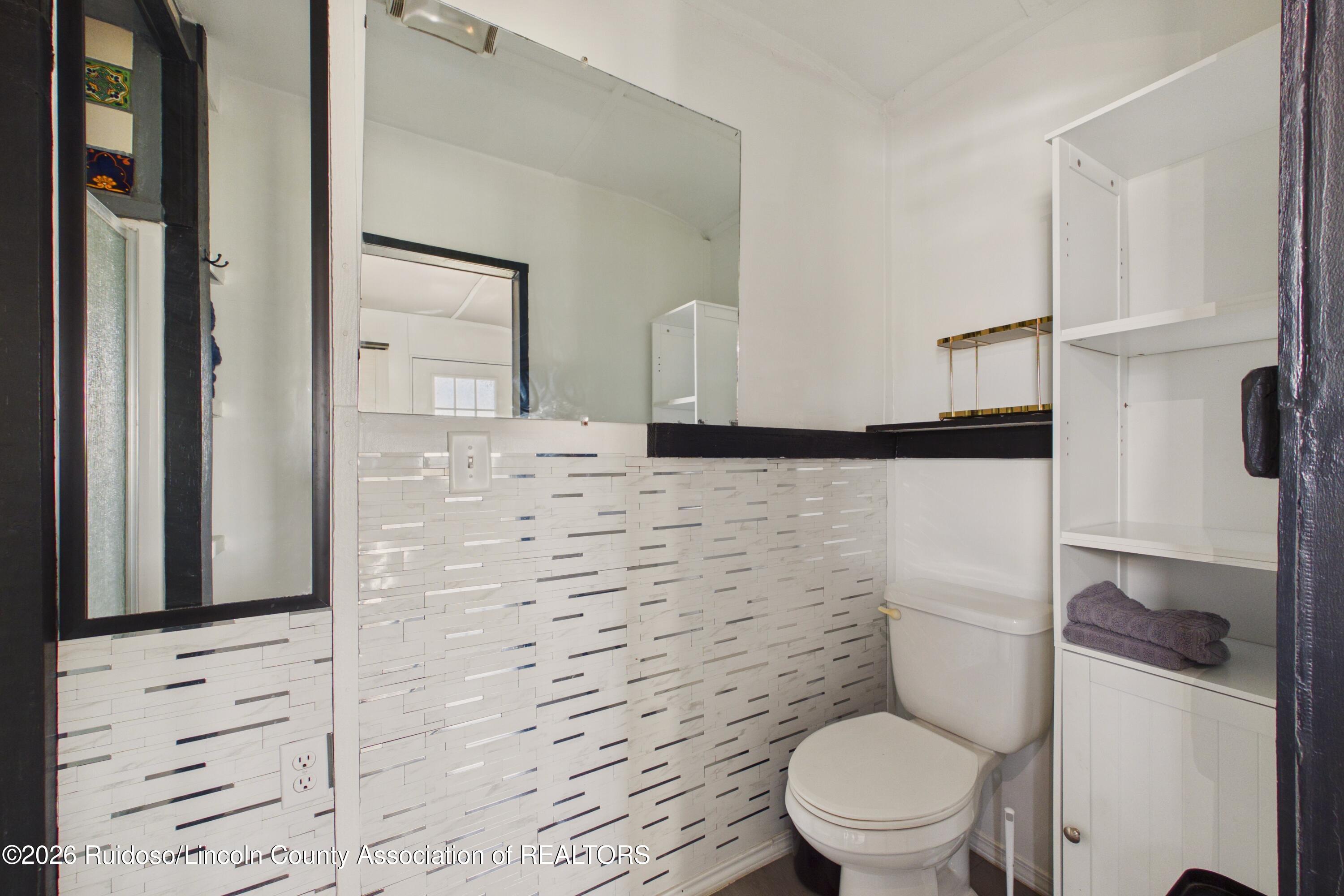 Bathroom with a white toilet, large mirror, built-in shelving, and patterned tile wainscoting.