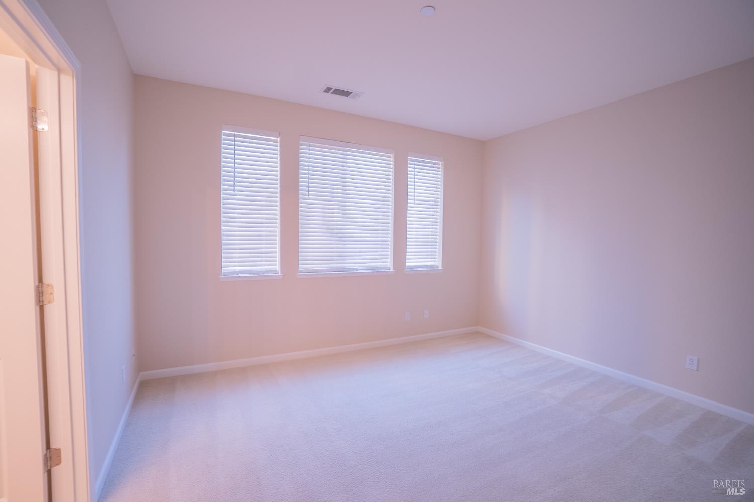 Empty carpeted room with three windows fitted with blinds.