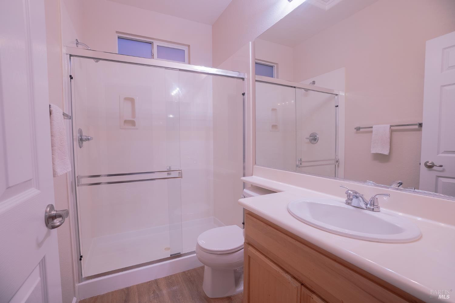 Bathroom with a glass-enclosed shower, wood vanity, and white sink.