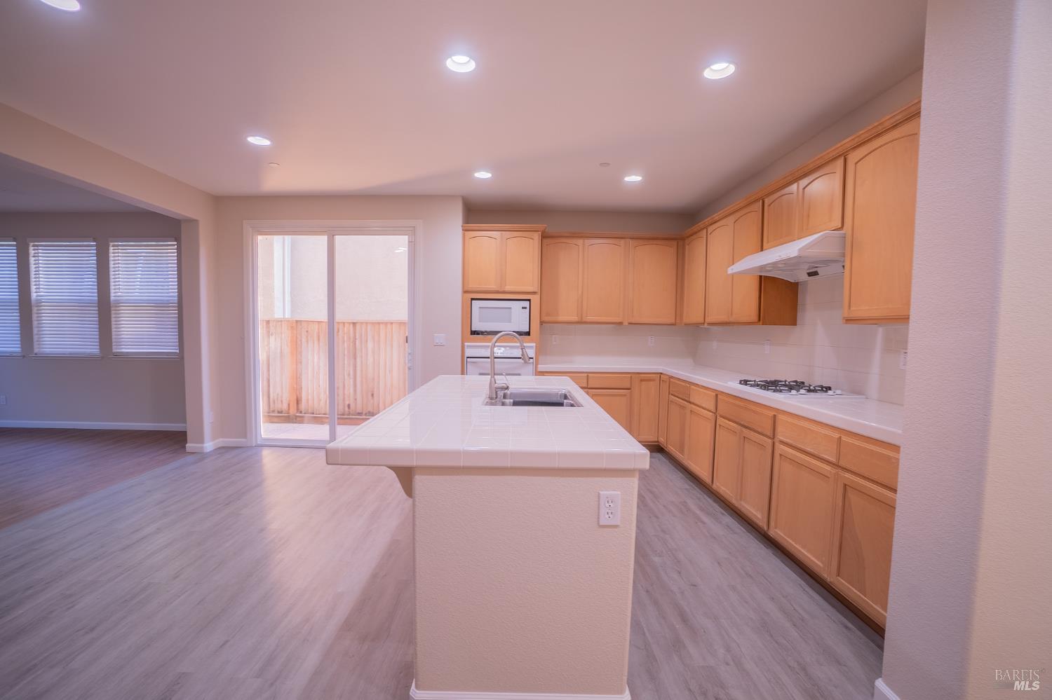 Kitchen with a large tiled island, honey-colored cabinets, and sliding glass doors.