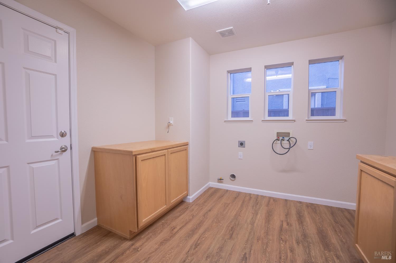 Laundry room with washer hookups, light wood cabinets, three windows, and wood-look flooring.