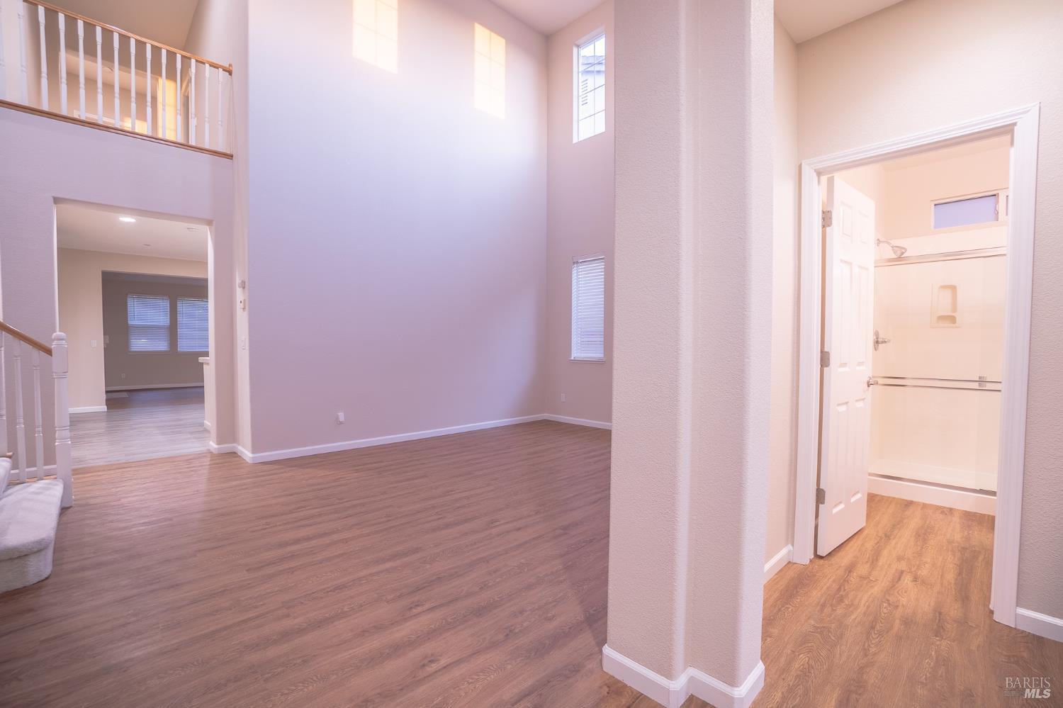 Two-story living room with wood-look flooring, staircase, and an open bathroom doorway.
