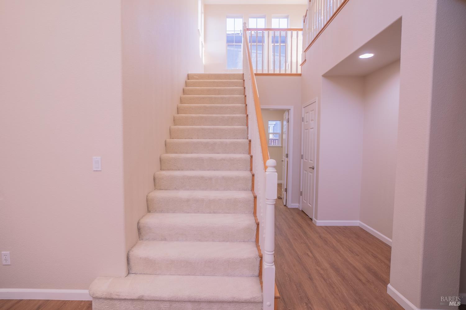 Carpeted staircase rises to a bright landing with tall windows and a wood handrail.