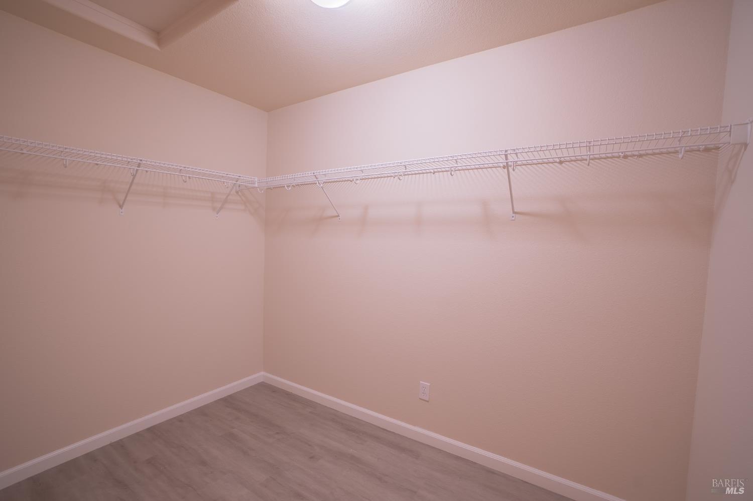 Empty walk-in closet with white wire shelving on two walls and gray flooring.