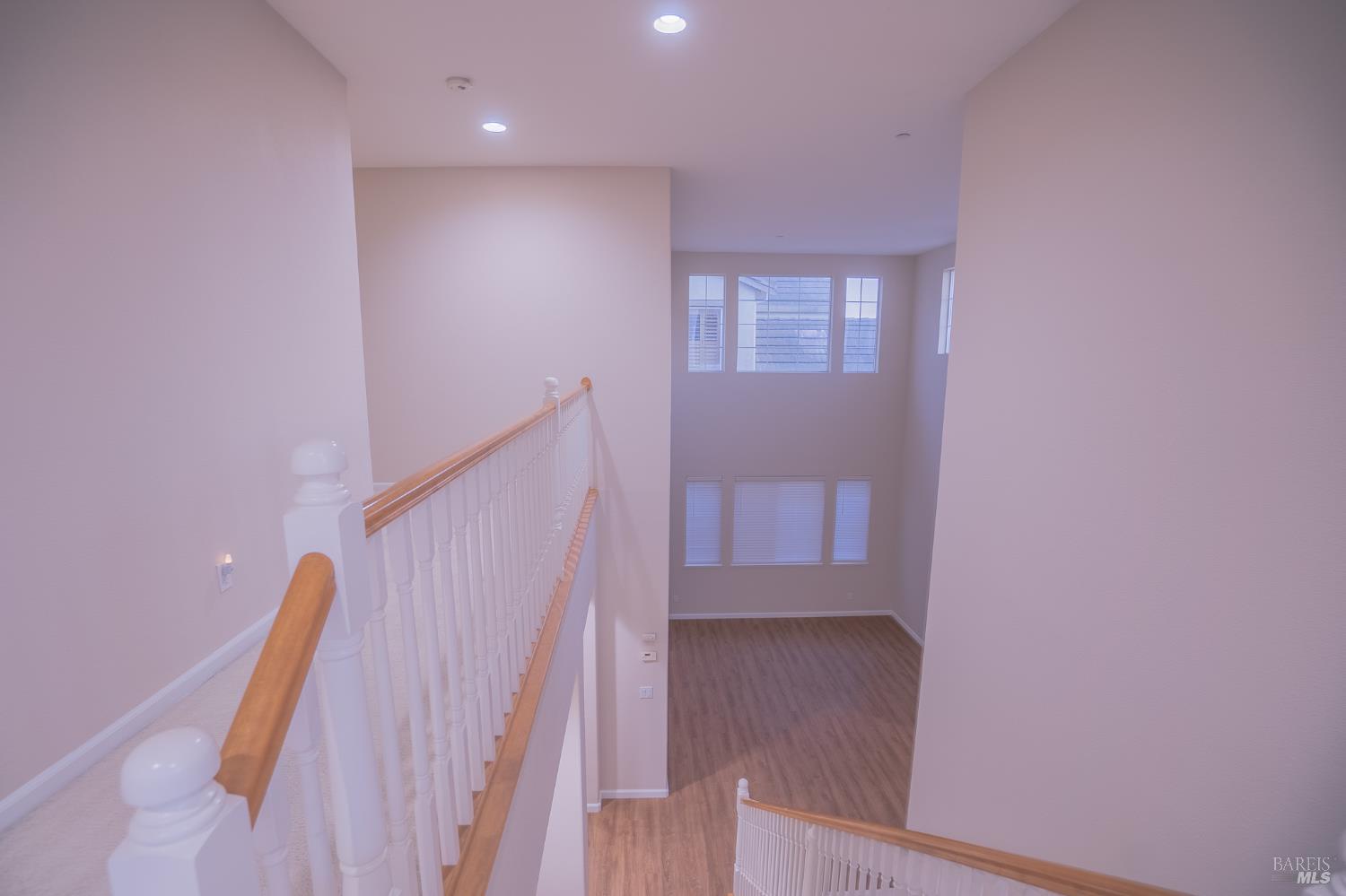 Staircase landing with white balusters, wood handrails, and a view into an empty room with large windows.