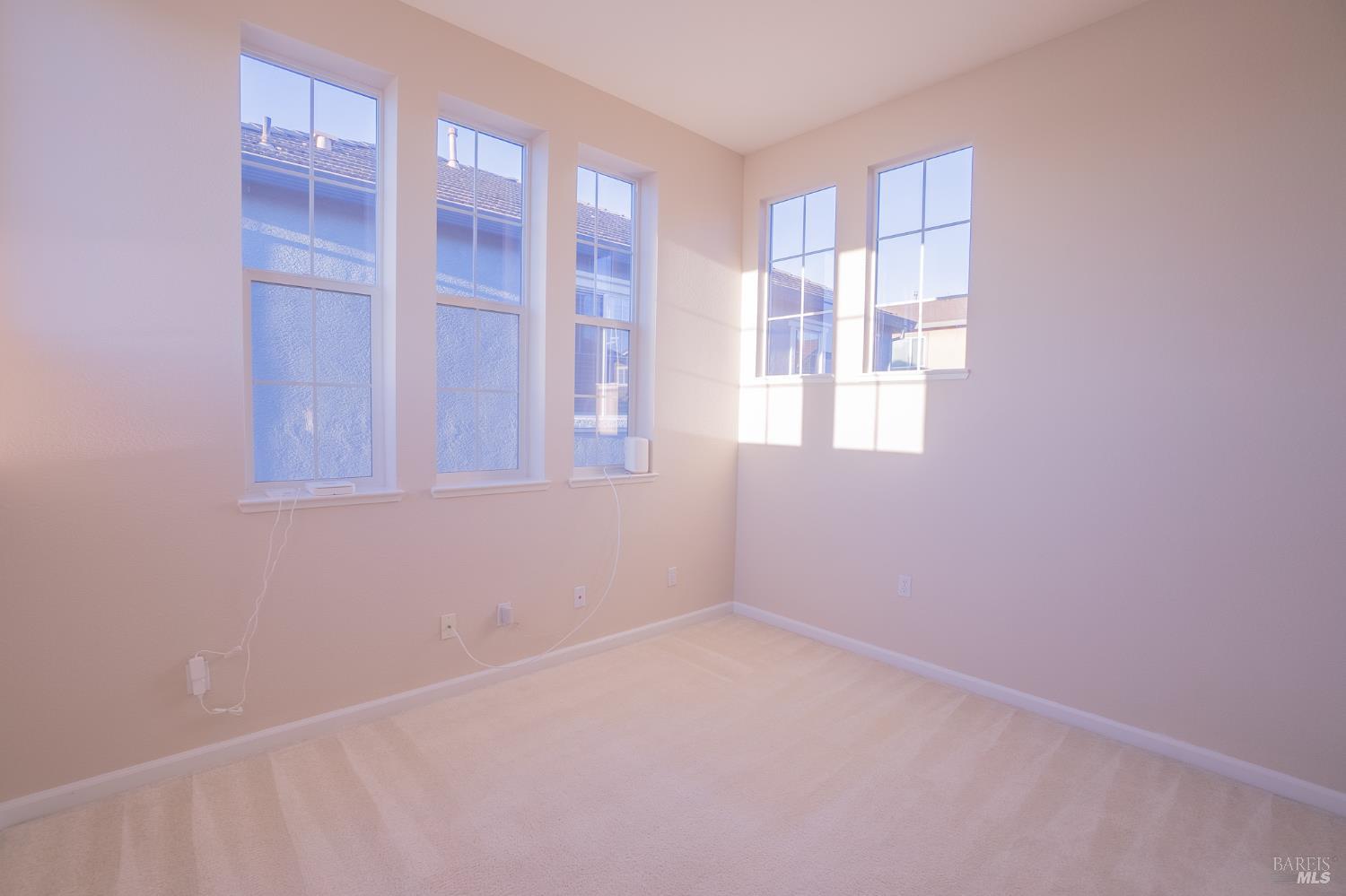 Empty carpeted room with tall windows and sunlight casting geometric shadows.