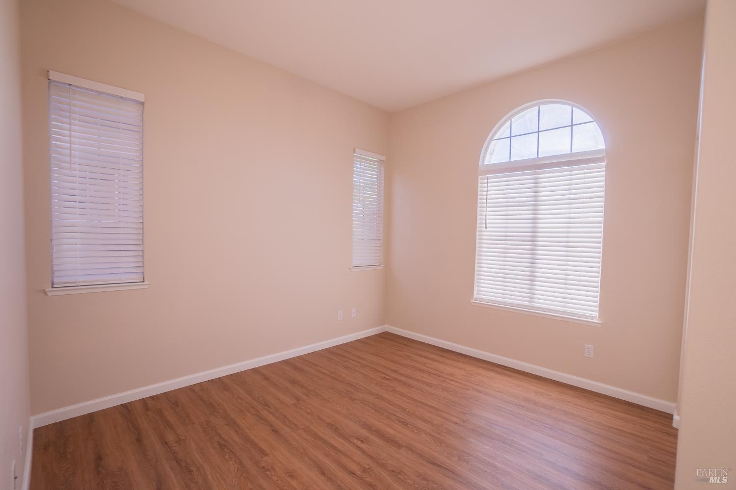 Empty room with wood-look flooring and three windows, including a large arched window.