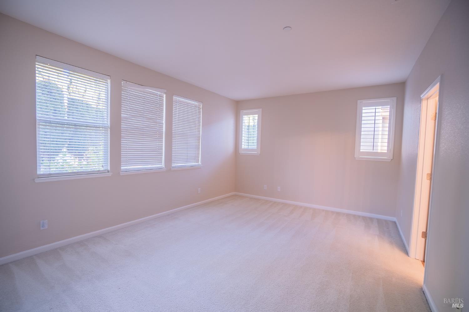 Empty carpeted bedroom with five shuttered windows and an open doorway.