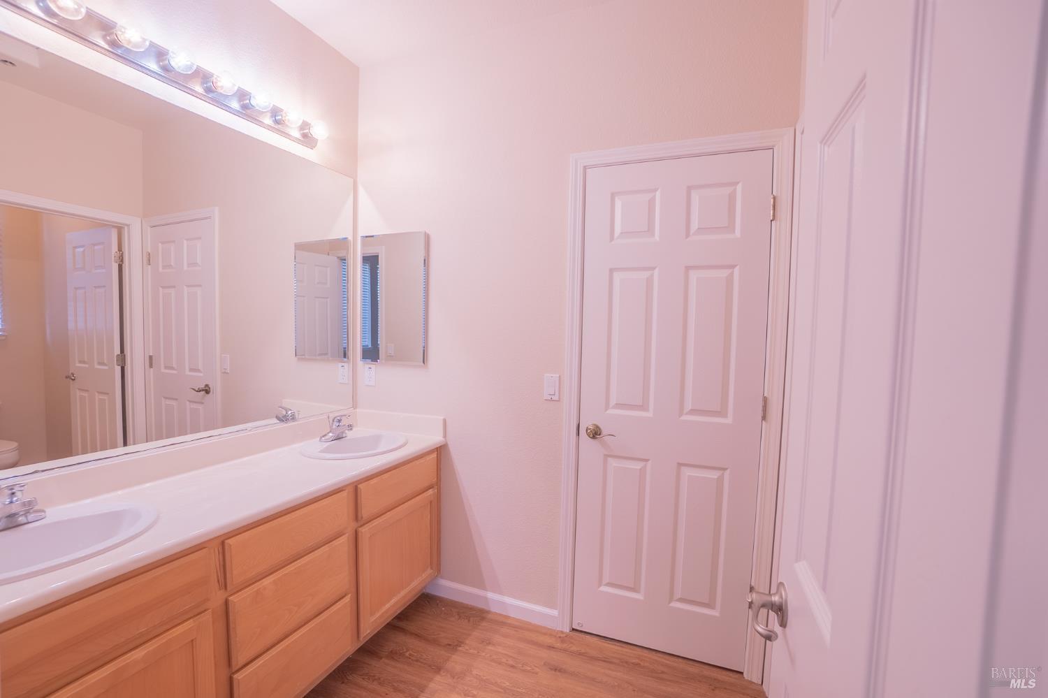 Bathroom with a double-sink vanity, wood cabinets, and mirrored wall.
