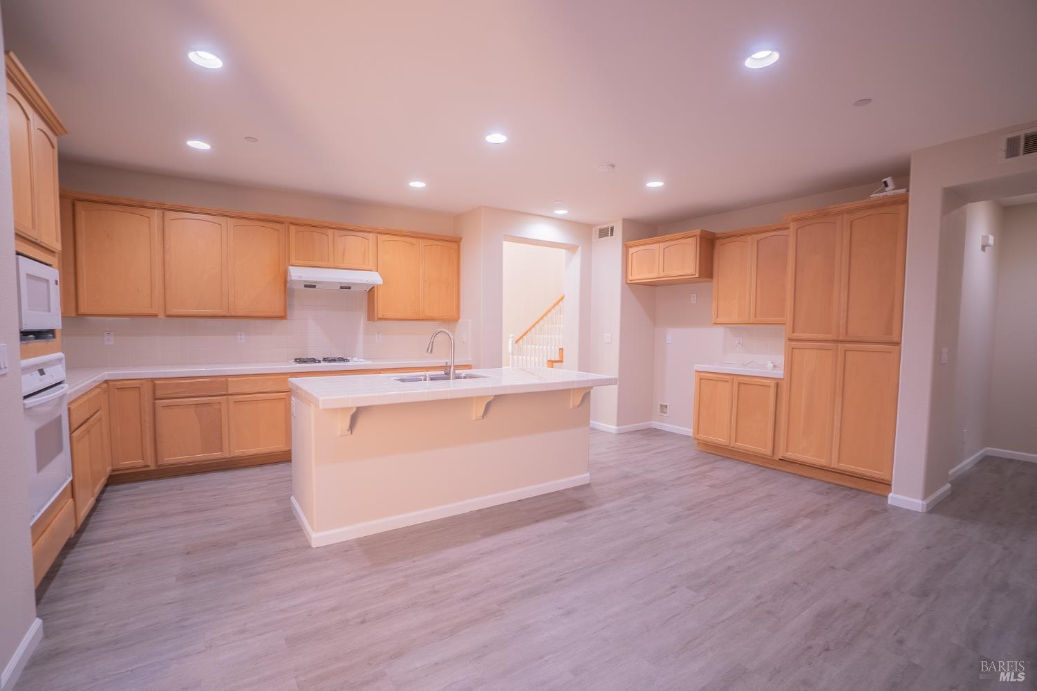 Kitchen with a large island, light wood cabinets, and gray plank flooring.