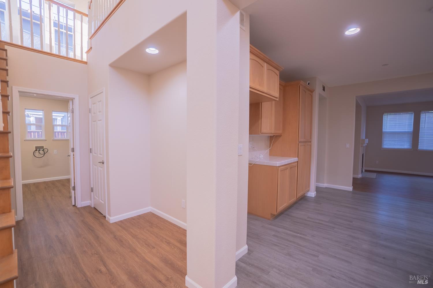 Entry hall with a staircase, tall windows, and built-in wood cabinetry opening to a living area.