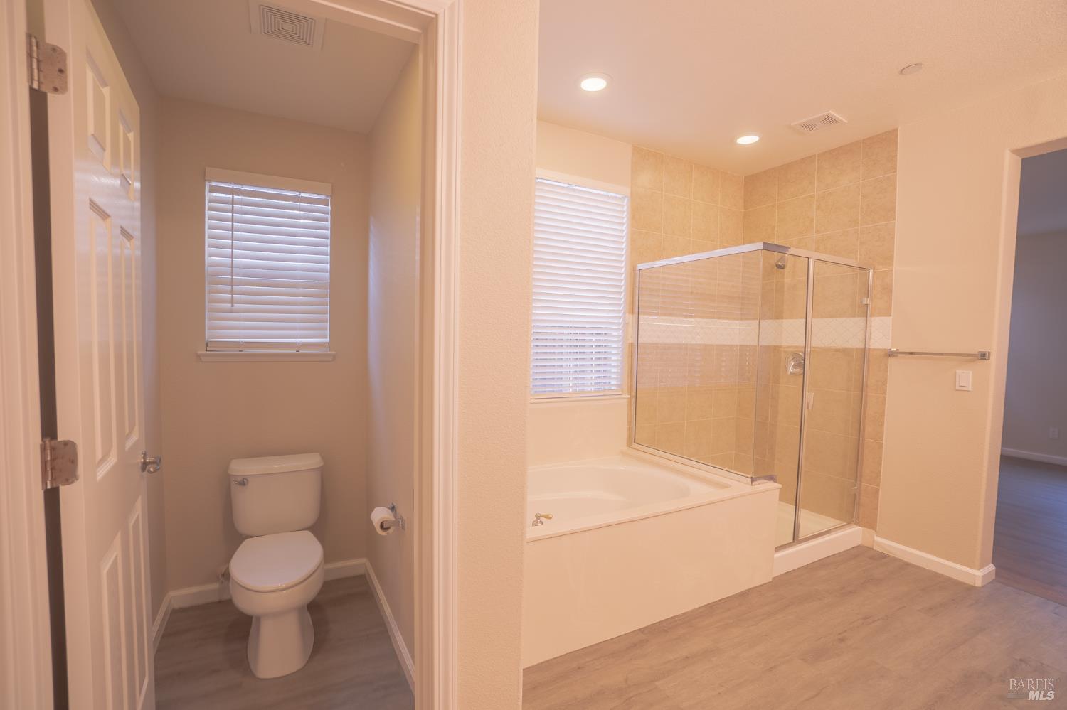 Bathroom with a tiled tub and glass shower enclosure beside a separate toilet room.