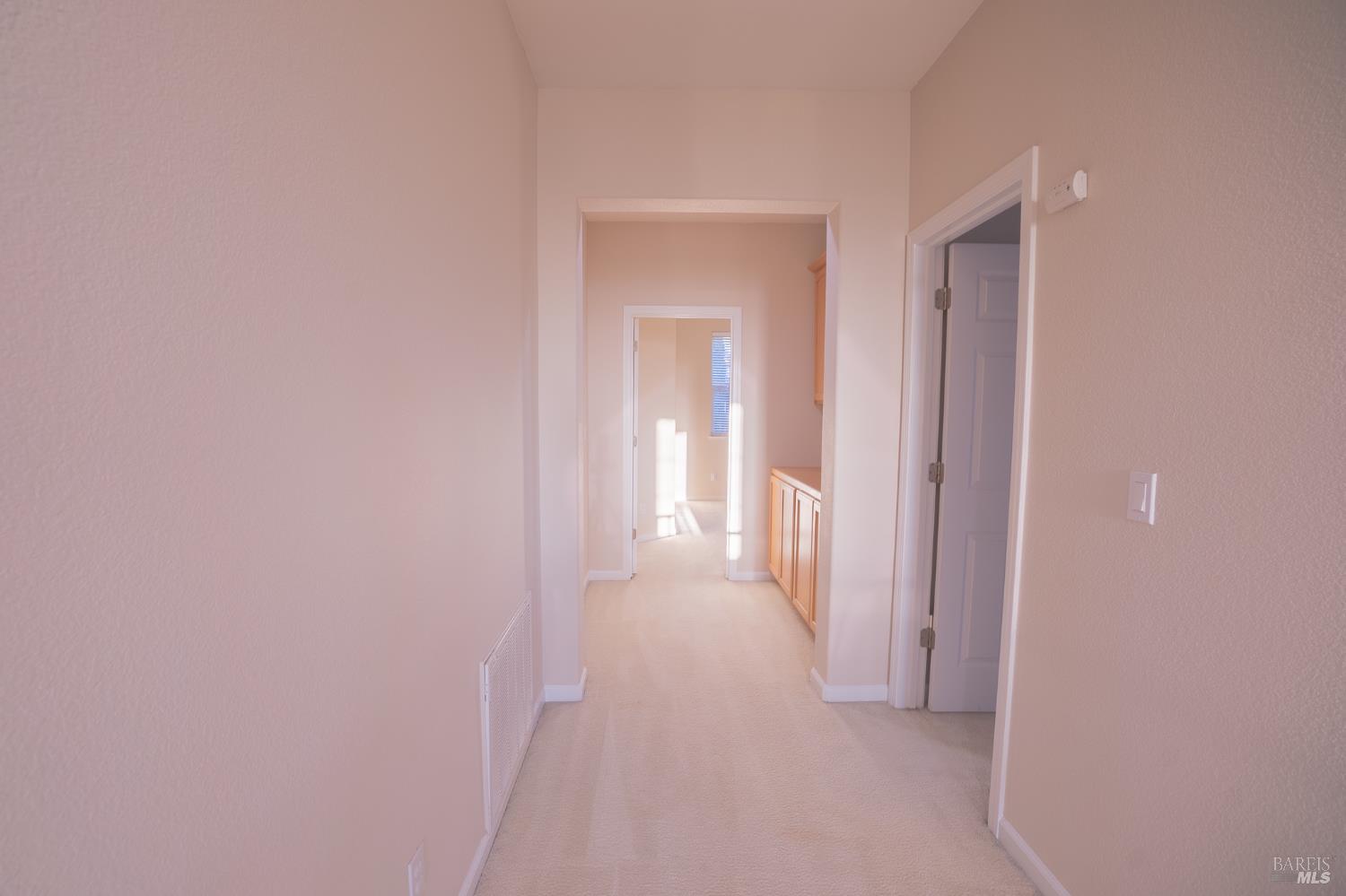 Carpeted hallway with white trim, an open doorway, and light wood cabinets.