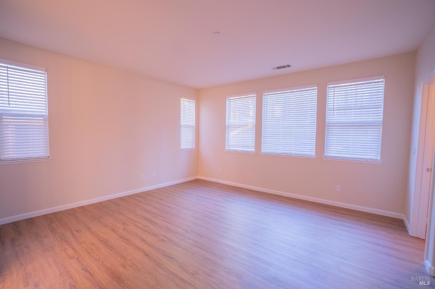 Empty room with wood-look flooring and several windows fitted with white blinds.