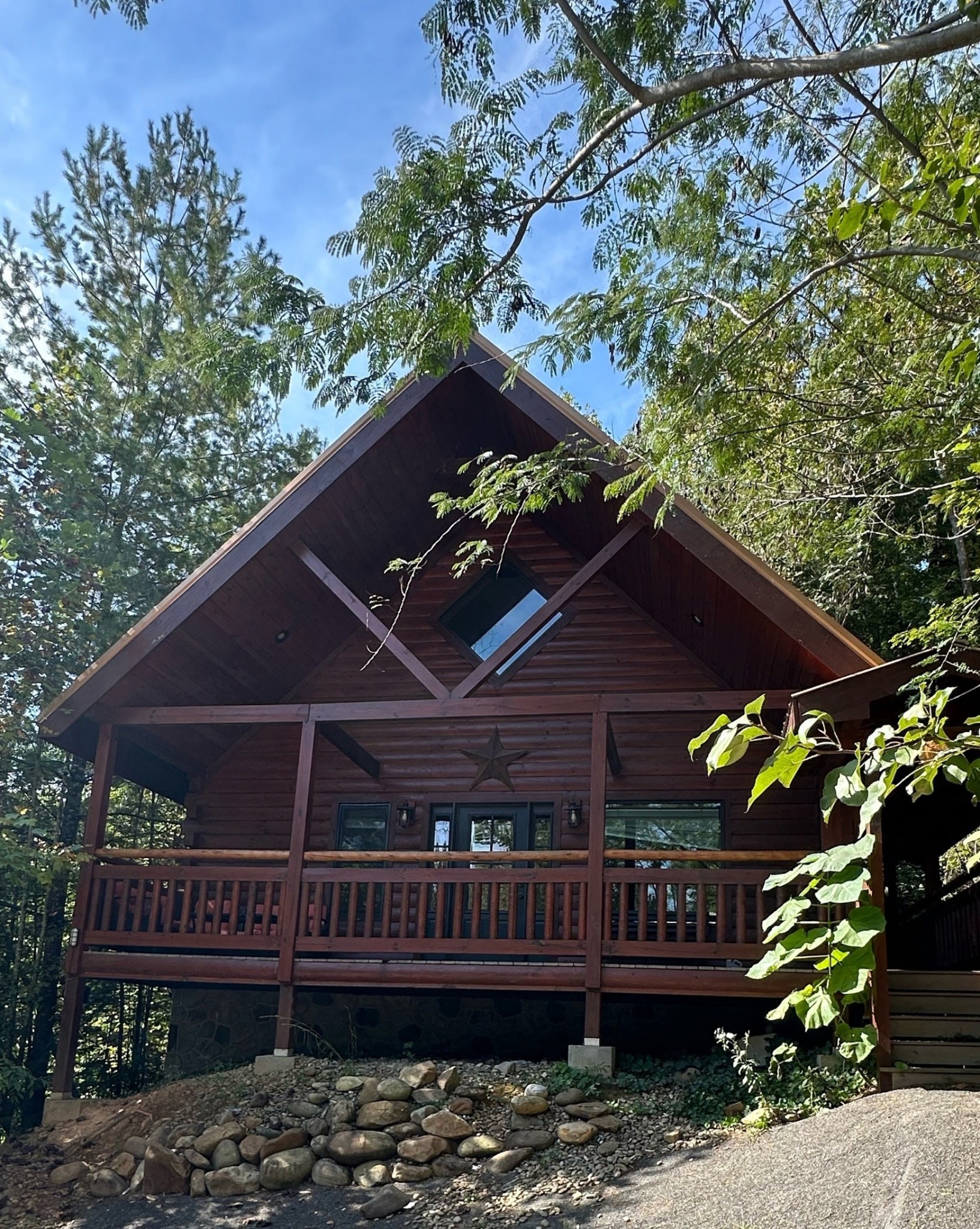 Wooden cabin with a steep gabled roof and covered porch among trees.