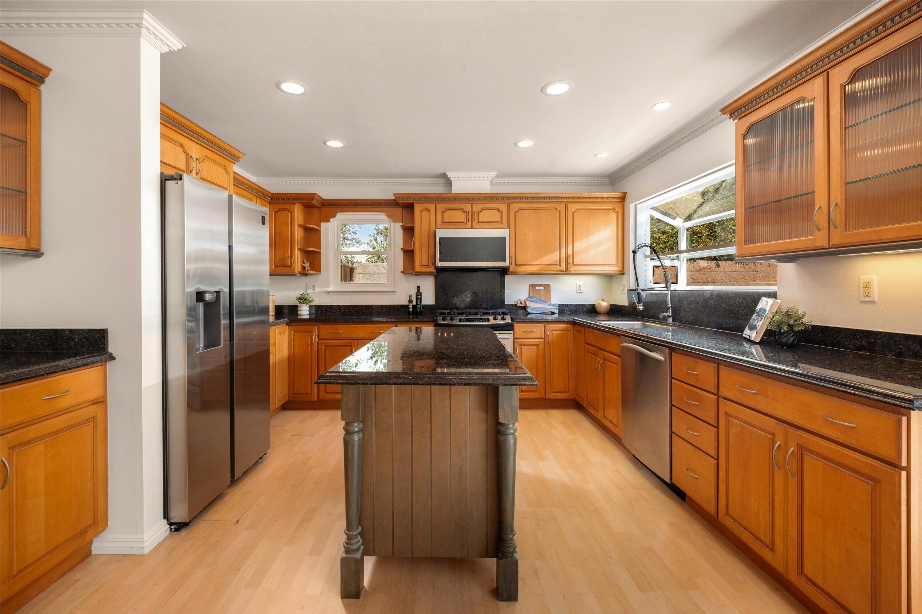 Kitchen with warm wood cabinetry, dark stone counters, a central island, and stainless steel appliances.