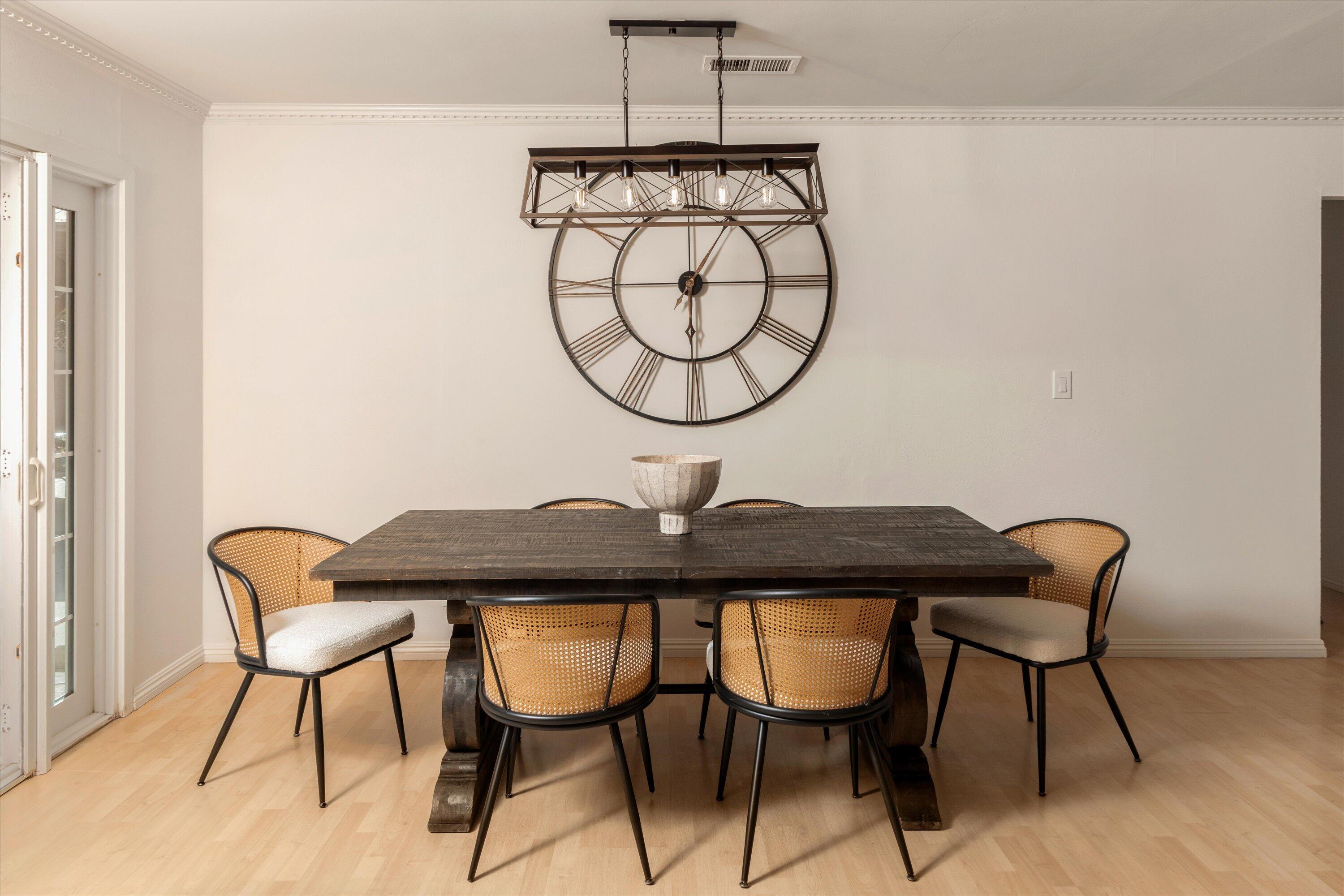 Dining room with a dark wood table, cane-back chairs, and a large round wall clock.