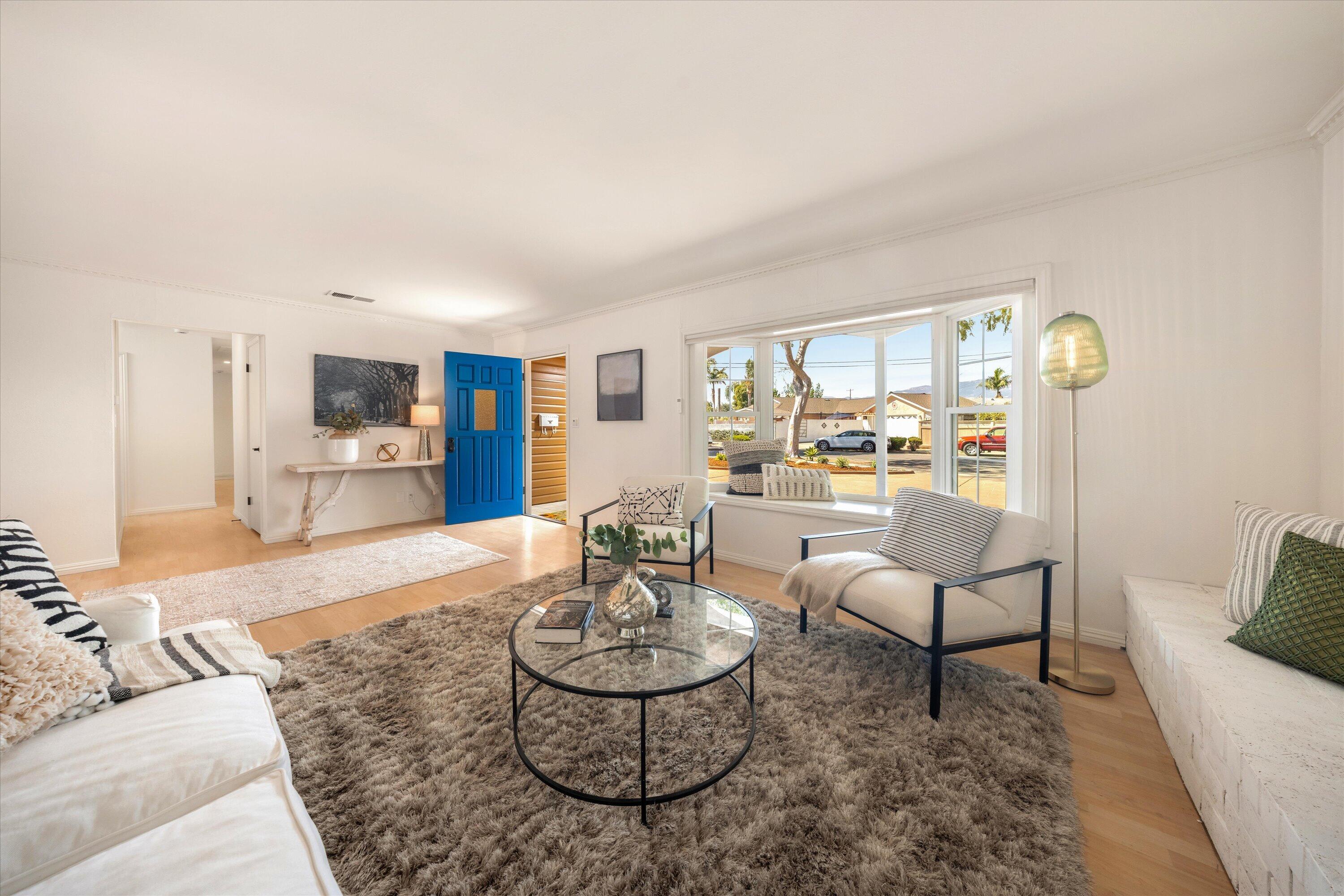 Furnished living room with a vivid blue front door, large windows, and a round glass coffee table.