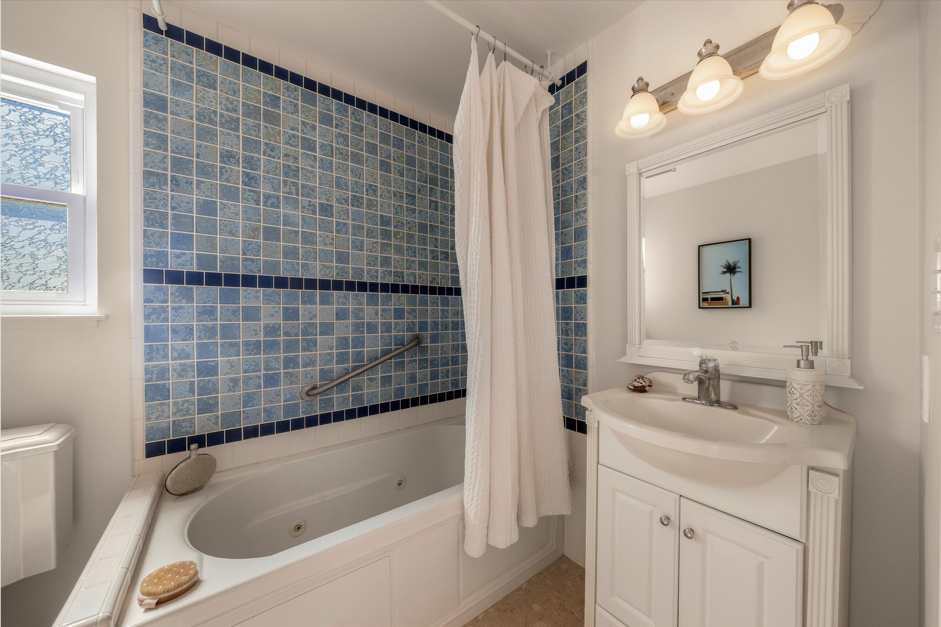 Bathroom with a jetted tub, blue patterned tile, and white vanity.