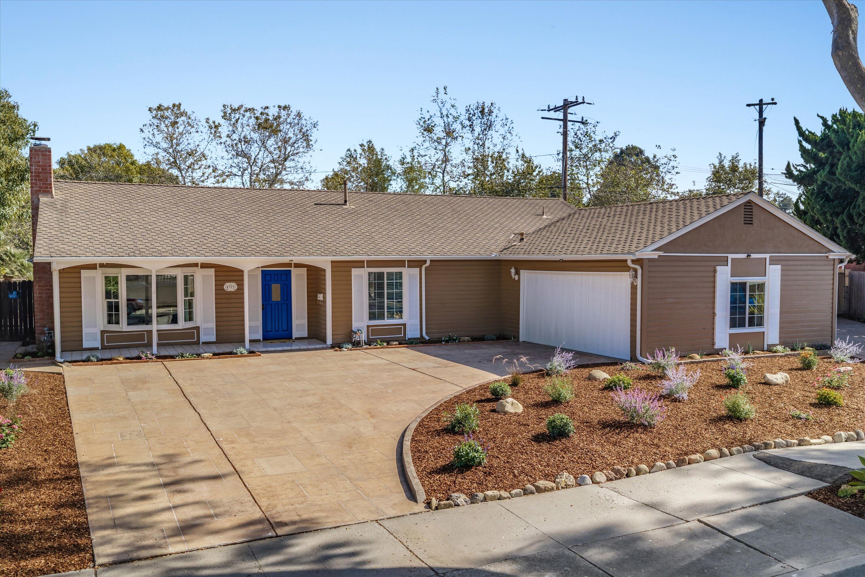 Single-story home with a bright blue front door, attached garage, and broad paved driveway.
