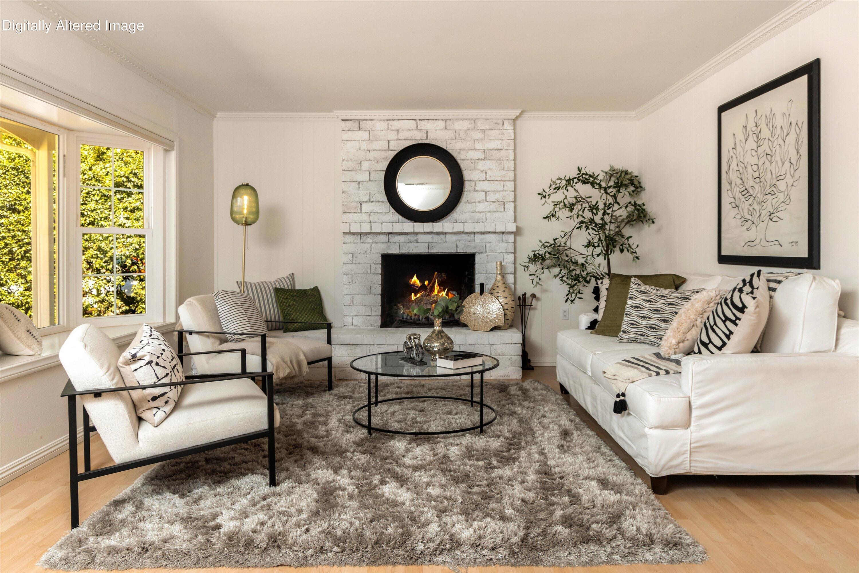 Staged living room with white sofas, a brick fireplace, and large windows.