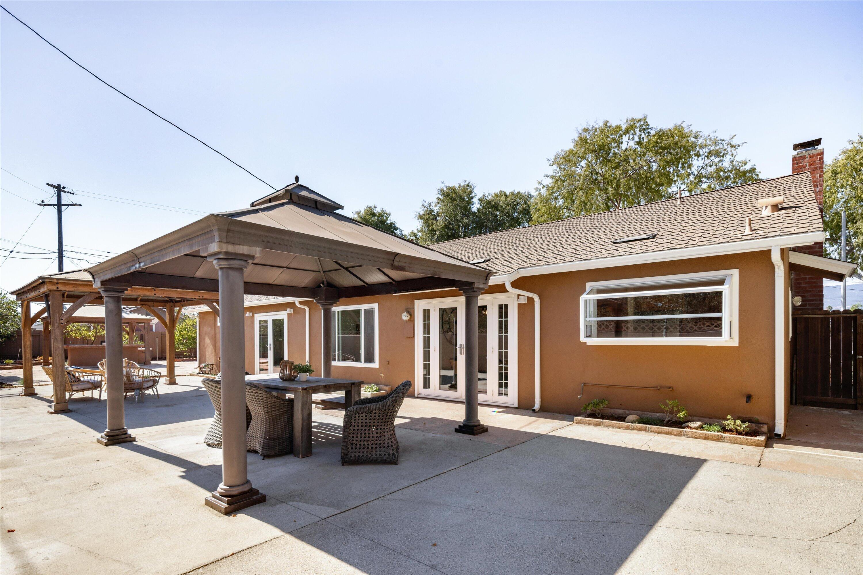 Rear patio with a large covered pavilion, outdoor dining furniture, and a second wooden shade structure.