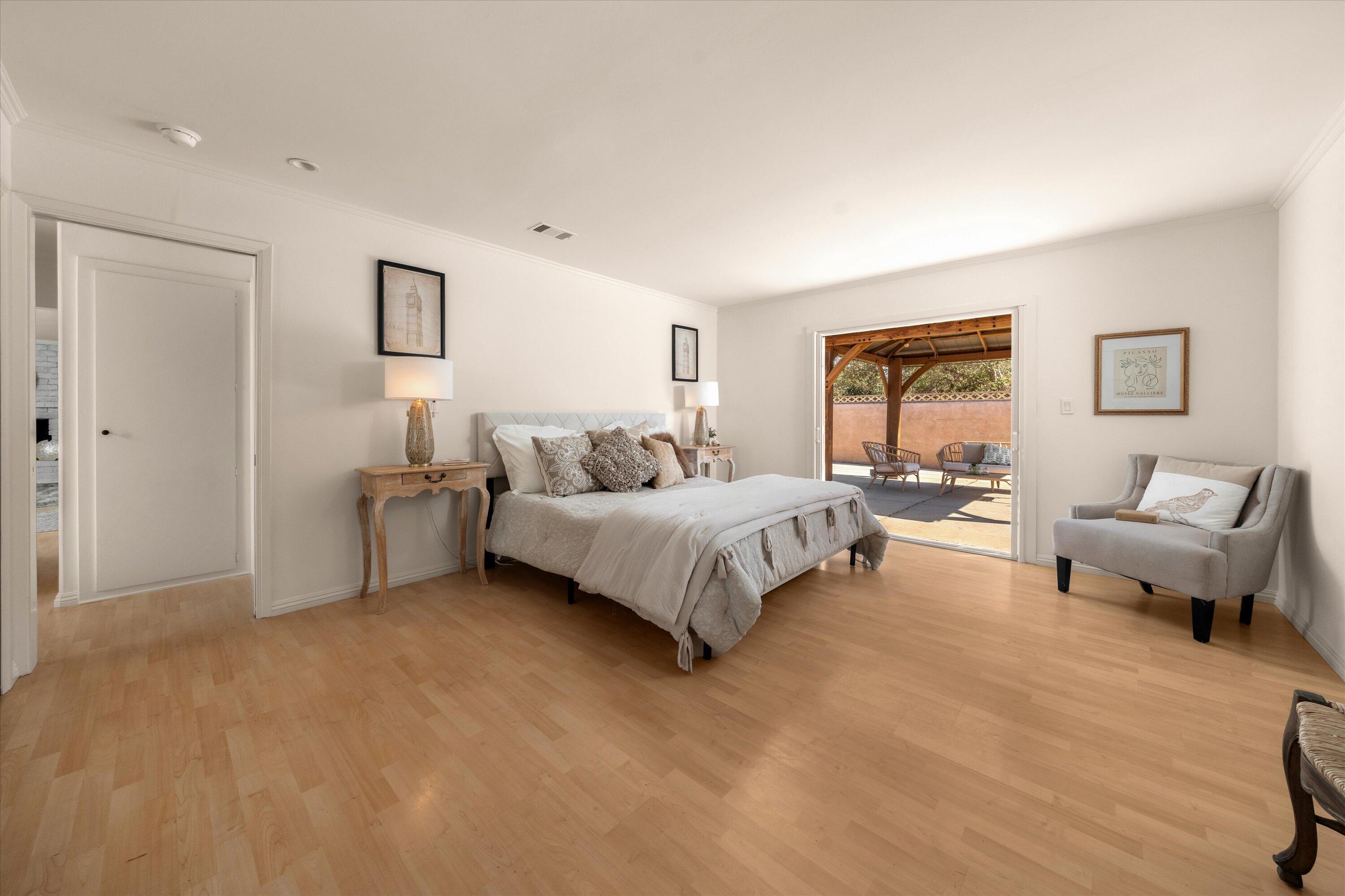 Staged bedroom with pale wood floors, a large bed, and doors opening to a covered patio.