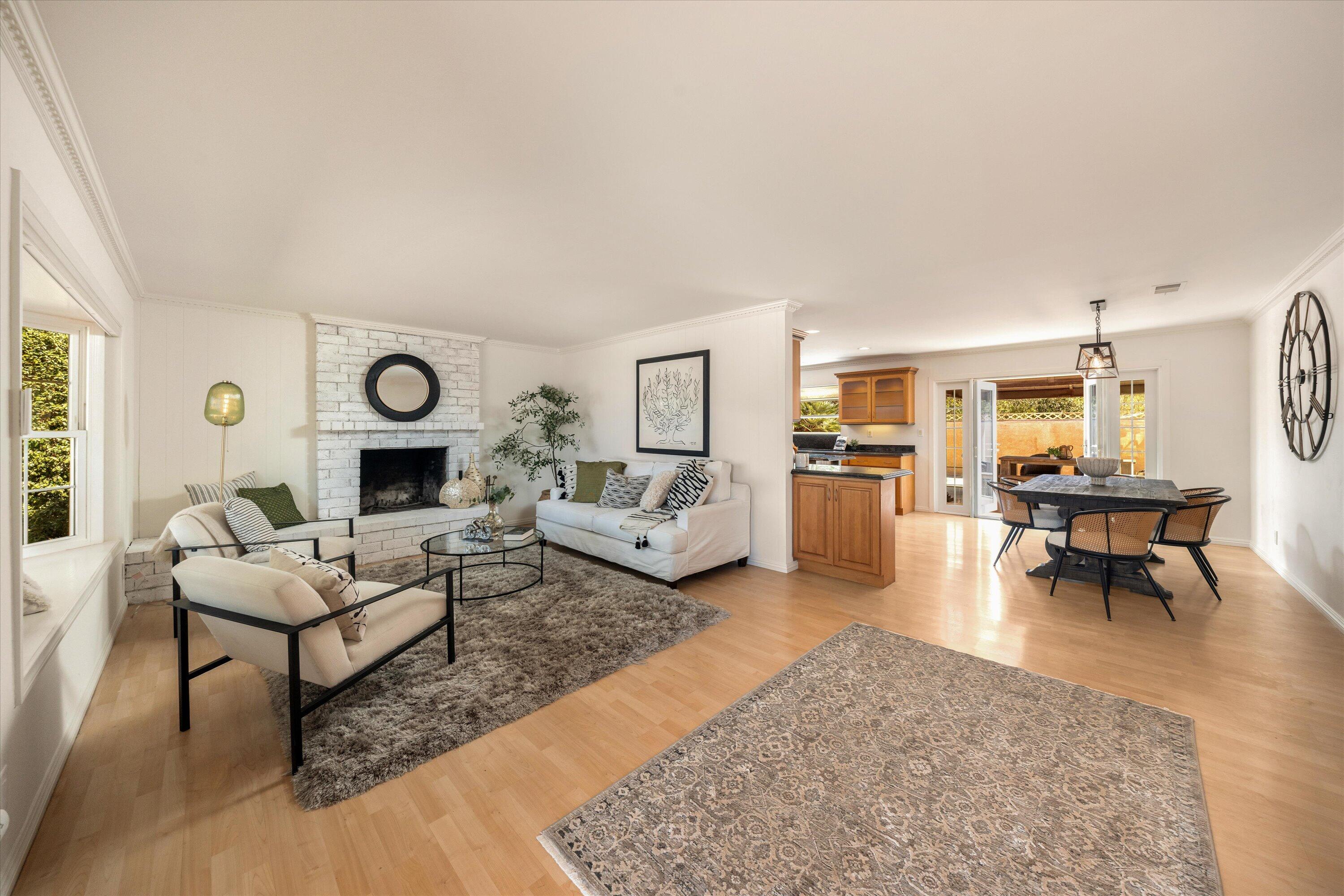 Staged living and dining room with a white brick fireplace, light wood floors, and open patio doors.