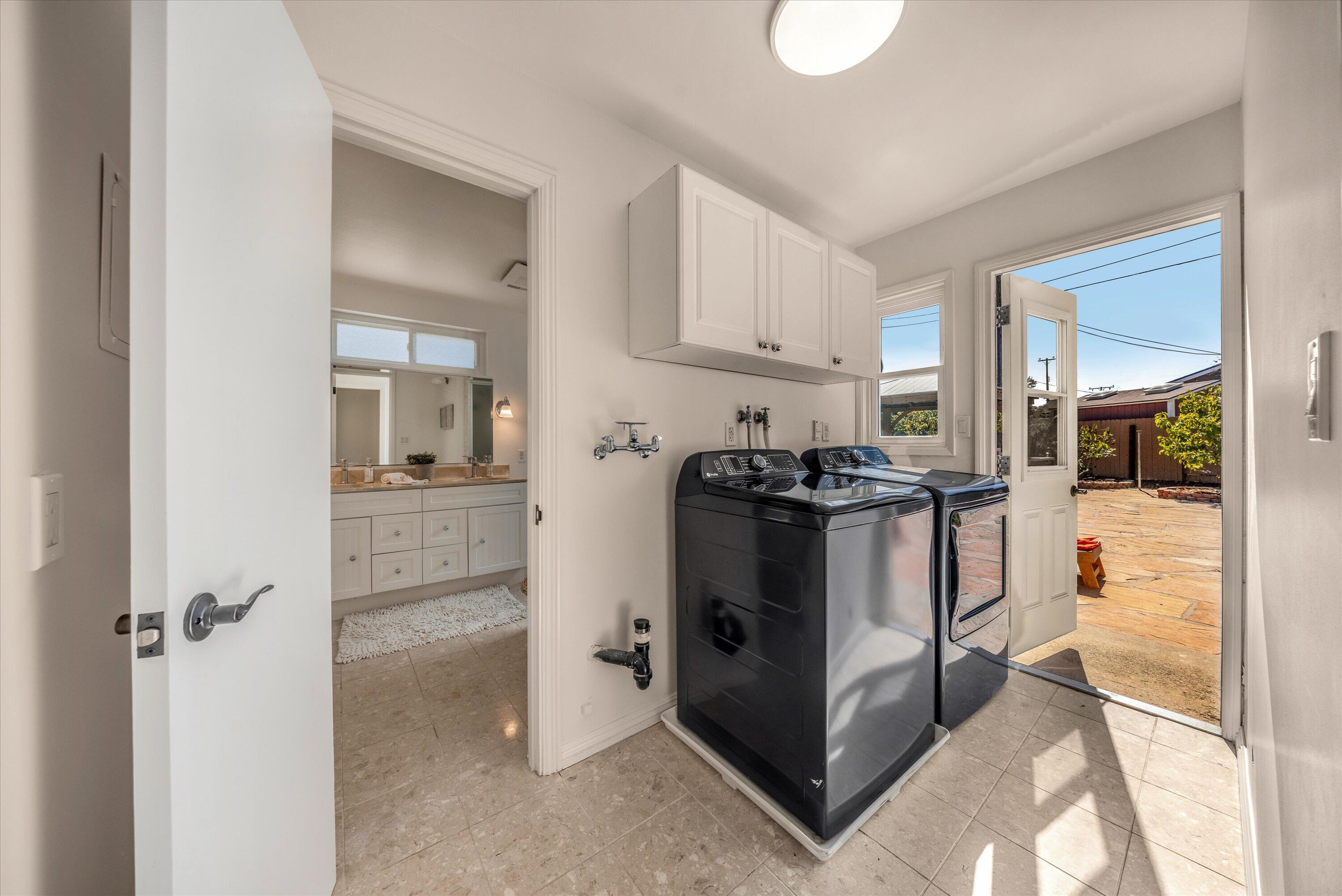 Laundry room with dark washer and dryer, white cabinets, and an open door to the patio.