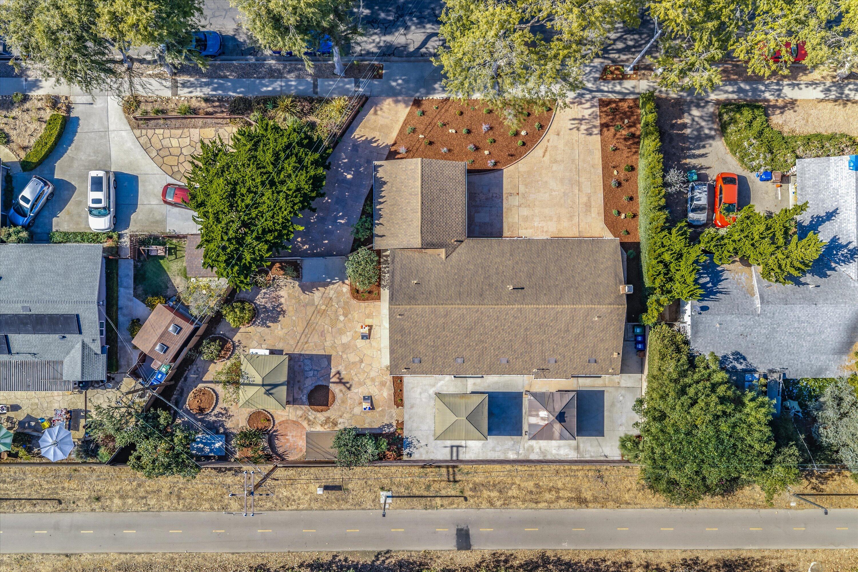 Aerial view of a house with paved patios, landscaped grounds, and a road along the property.