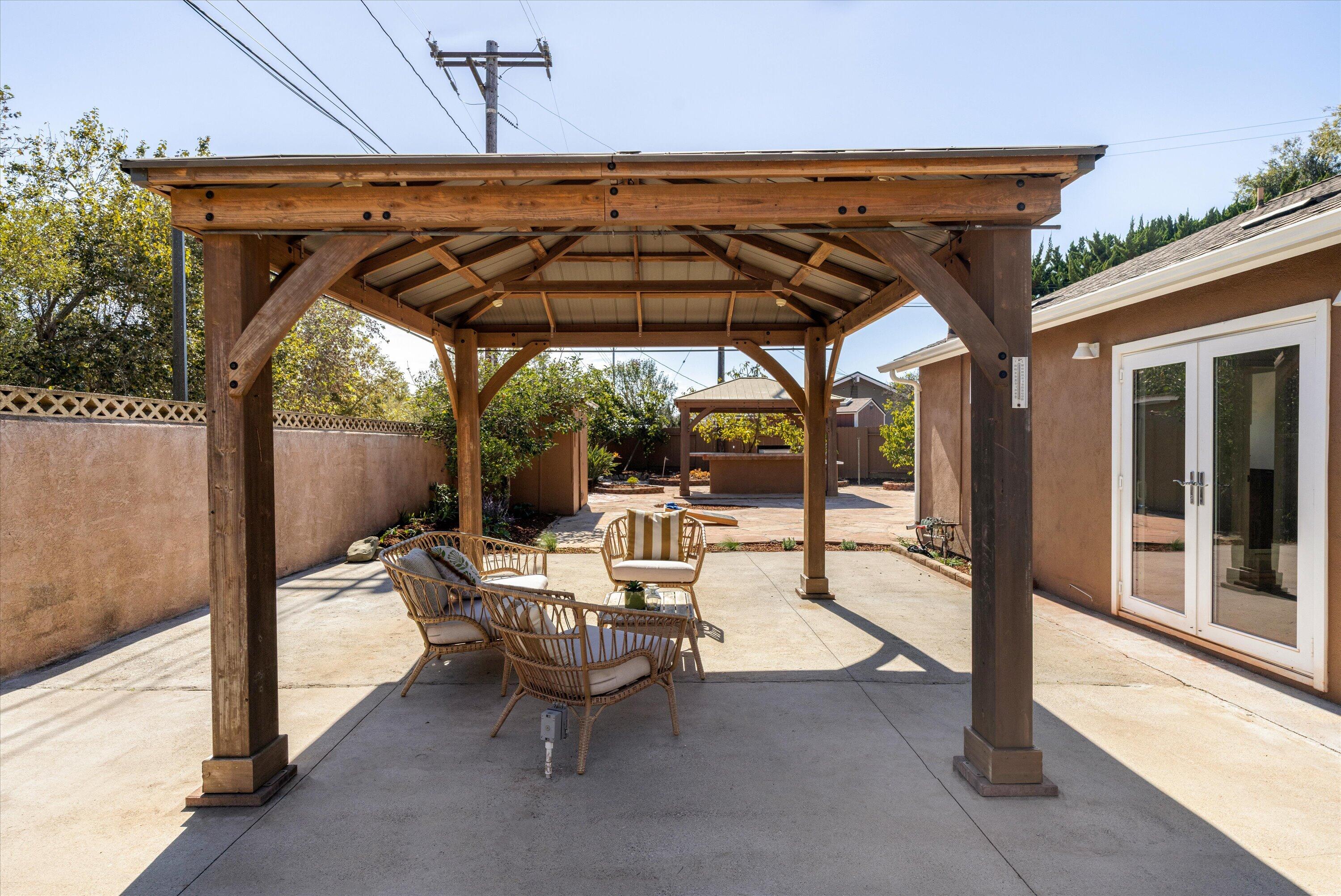 Backyard patio with timber pergola, wicker seating, and white French doors.