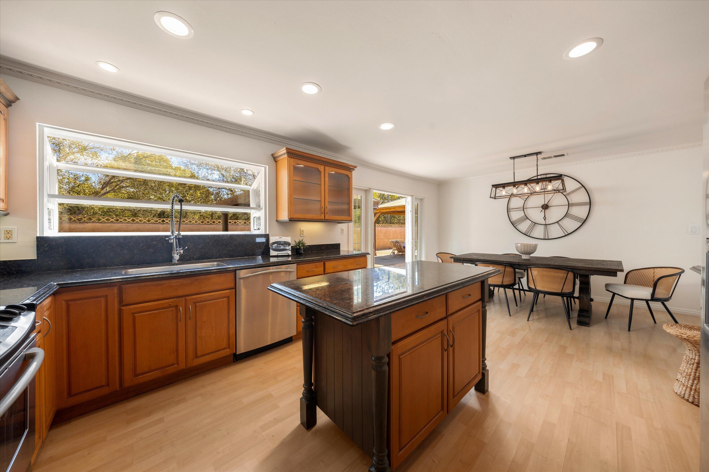Kitchen with a dark stone island, warm wood cabinetry, and an adjoining dining area with a large wall clock.