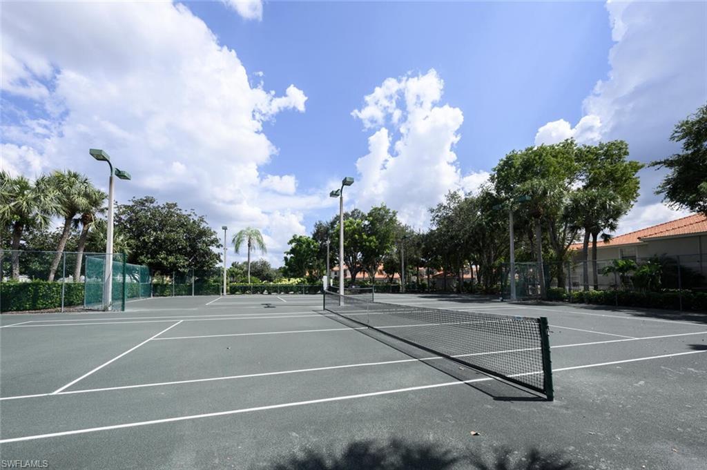 Outdoor tennis courts with black nets, surrounded by tropical trees and fencing.