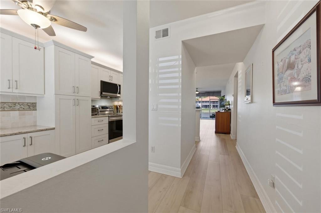 White kitchen with stainless steel appliances beside a hallway leading to a water view.