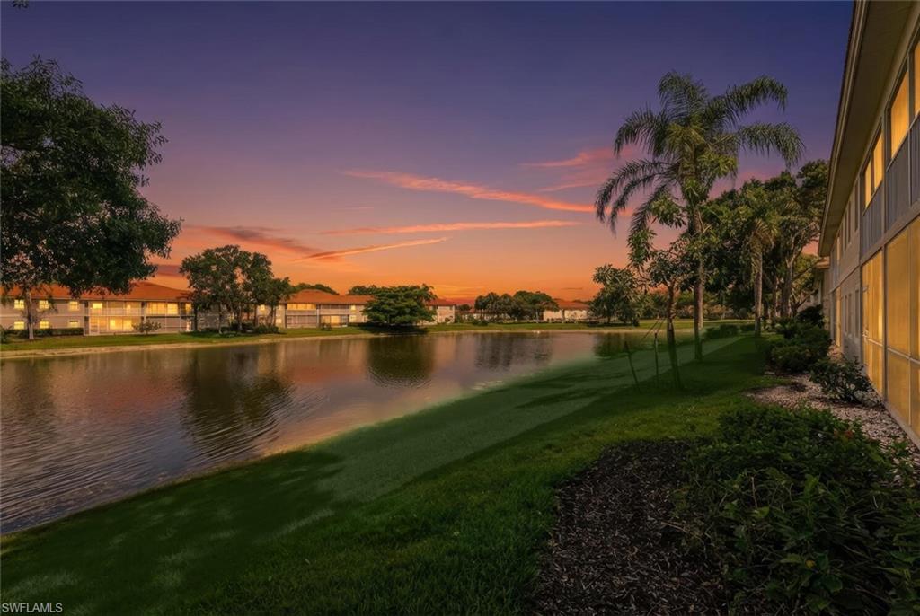 Residential buildings beside a landscaped canal at dusk, with palm trees and sunset colors reflected in the water.