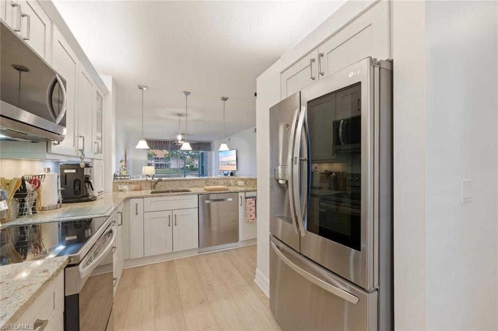 Kitchen with white cabinets, granite counters, stainless steel appliances, and light wood flooring.